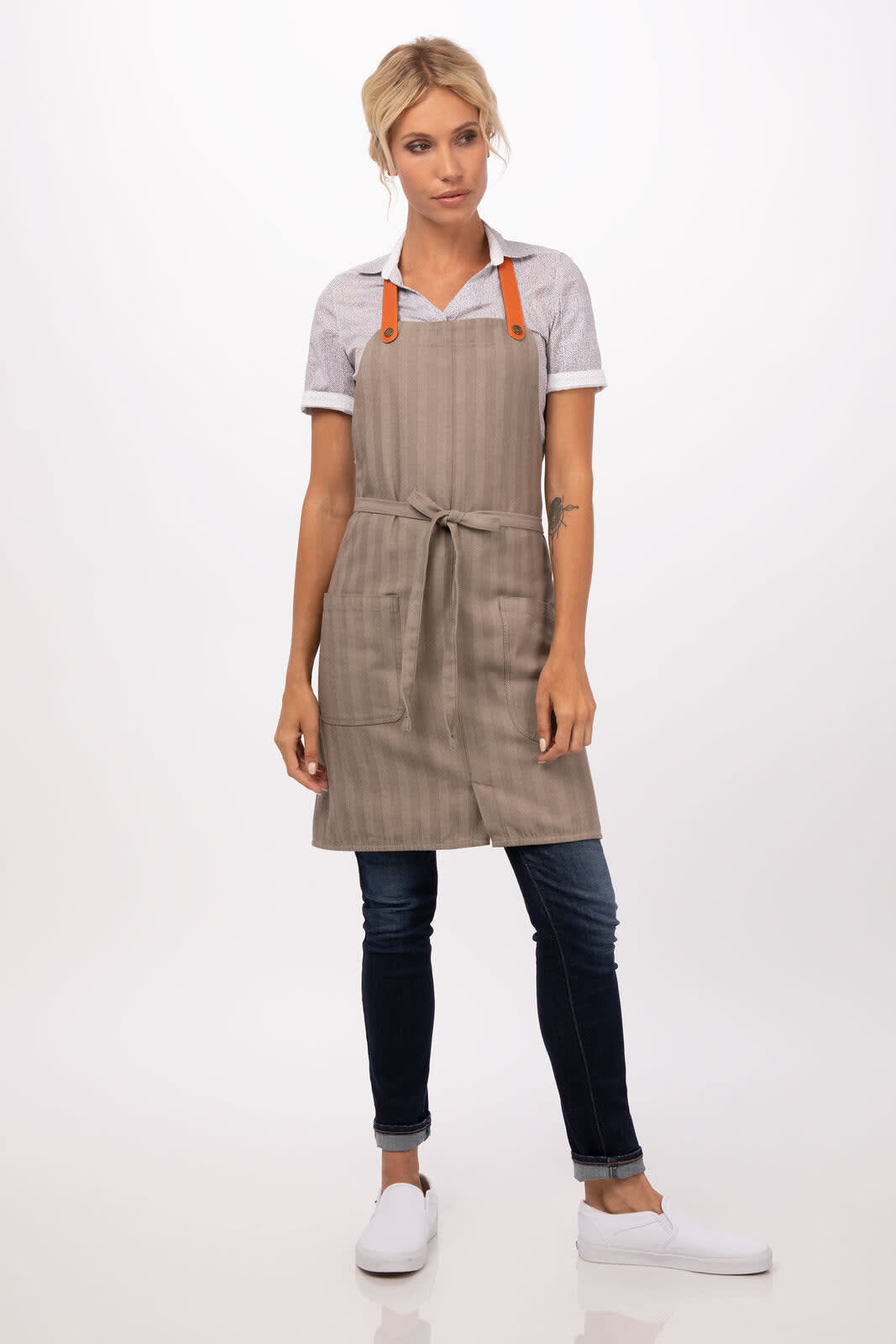 A beige striped bib apron with orange straps, styled on a model wearing a white shirt and dark jeans.