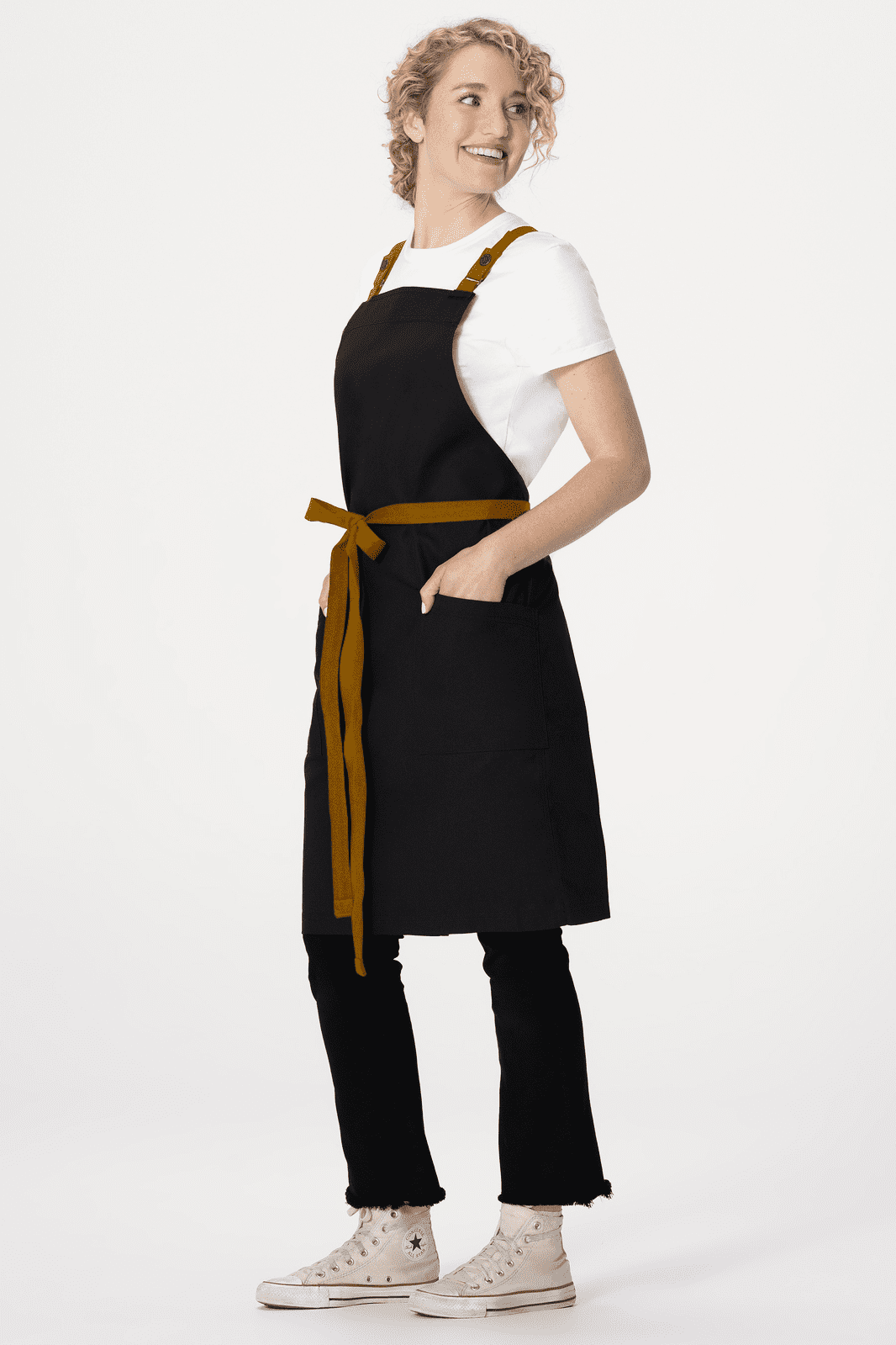 A black Lockharte cross back apron featuring a brown tie waist and pockets, worn over a white t-shirt.
