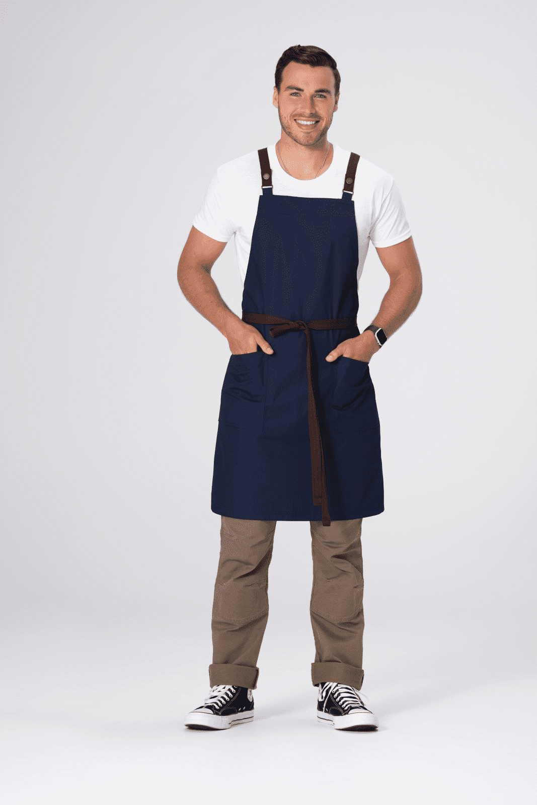 A man wearing a navy blue Lockharte Cross Back Apron with a brown belt, standing confidently with hands in pockets.