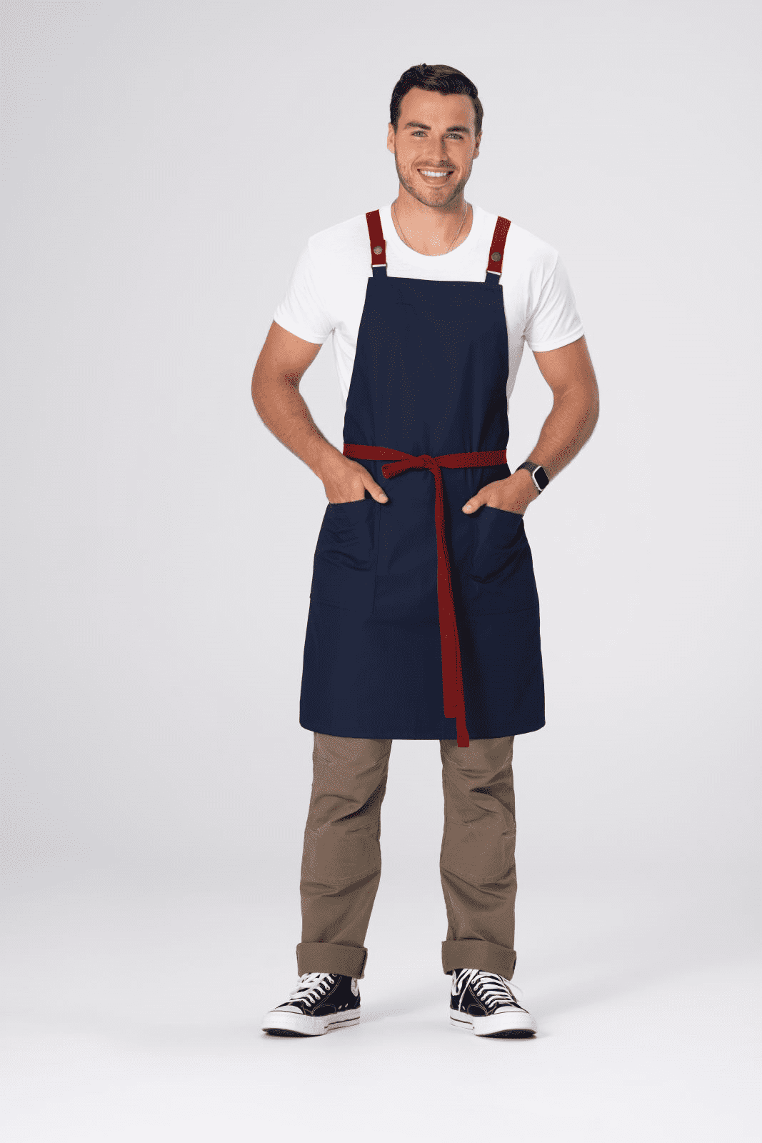 A navy blue apron with red straps and a belt, featuring two front pockets, worn by a smiling man.