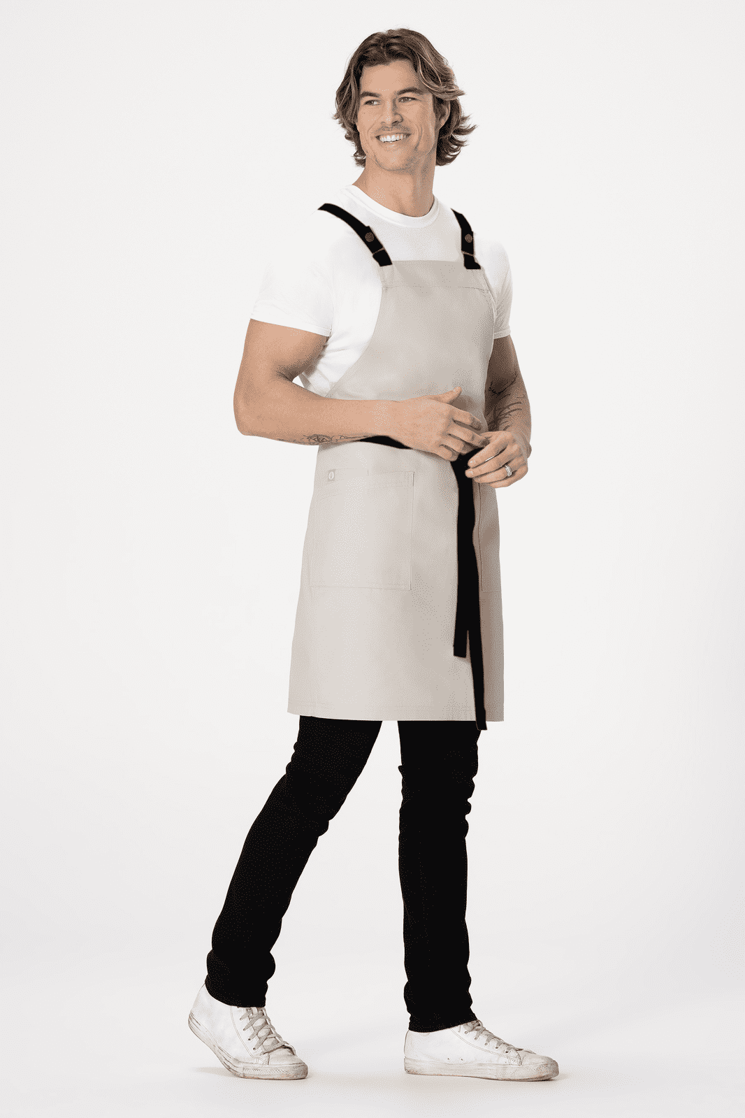 A light grey cross back apron with black straps worn by a person. The apron has a logo on it.