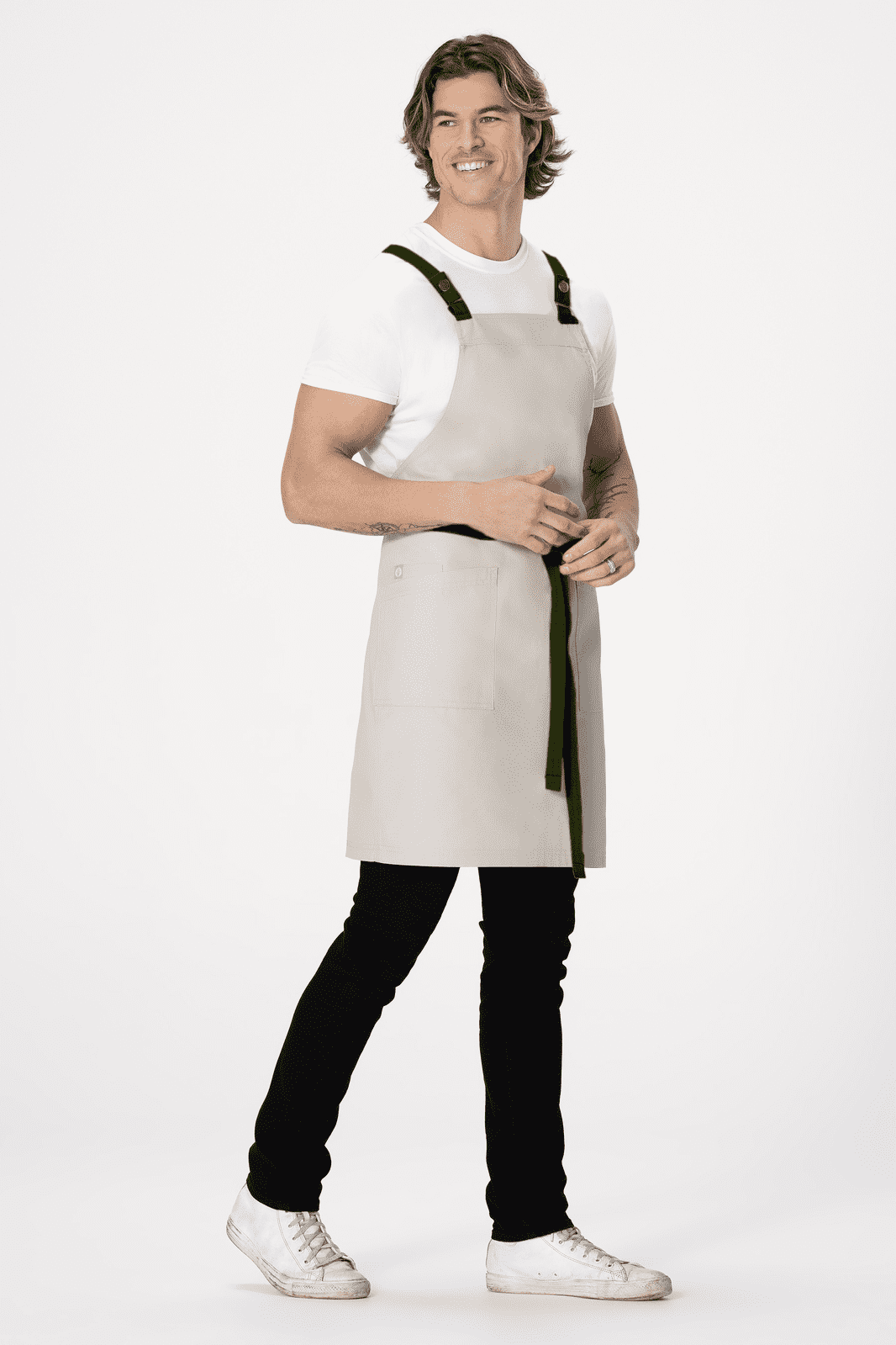 A light grey cross back apron worn by a model, featuring black straps, paired with black pants and white shoes.