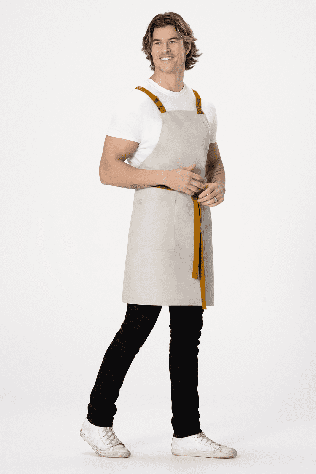 A man wearing a light grey cross back apron with brown straps, standing against a plain background.