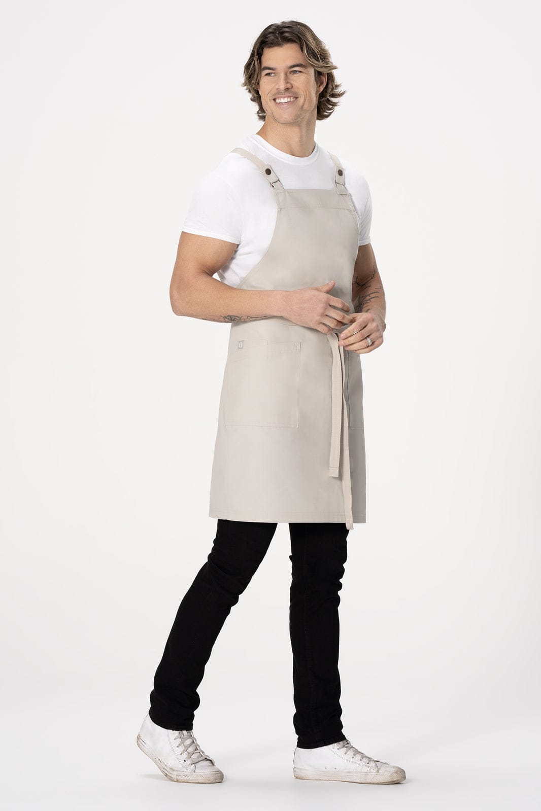 A light grey cross back apron worn by a model, featuring a logo and adjustable straps.