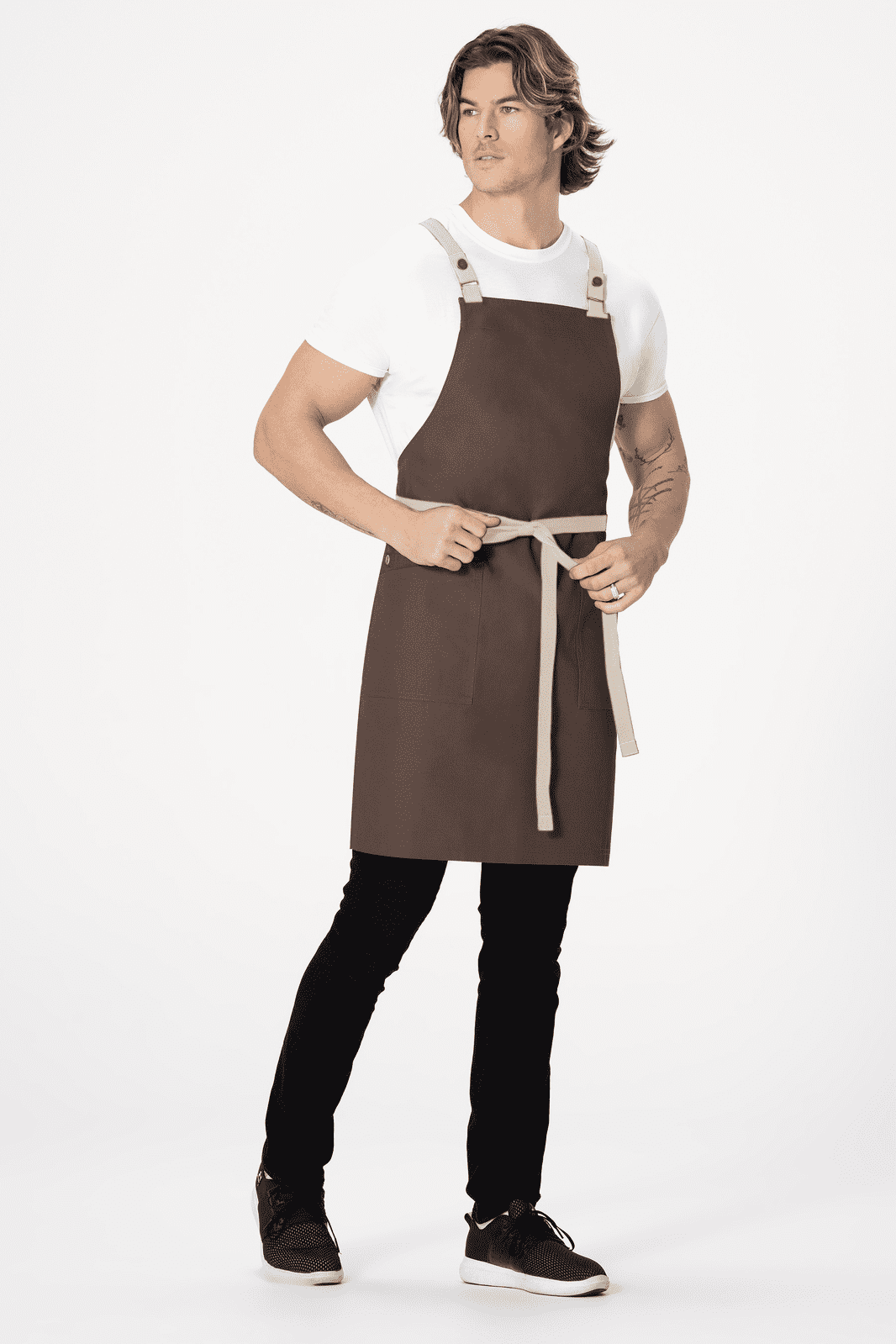 A brown cross back apron with adjustable straps and a waist tie, worn by a model against a plain background.