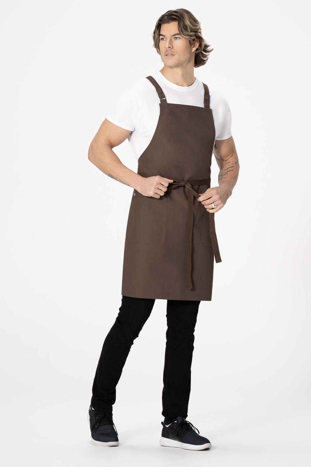 A brown cross back apron worn by a model, featuring adjustable straps and a tied waist.