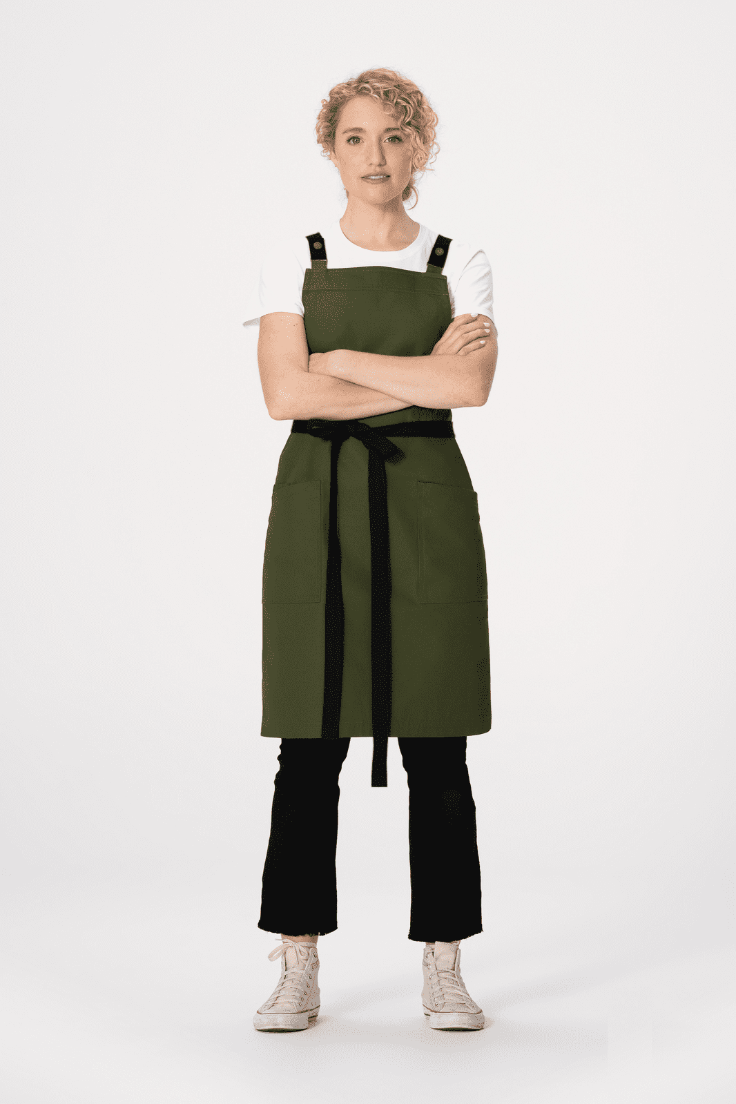 A green cross back apron with black straps, modelled by a person wearing a white t-shirt and black pants.