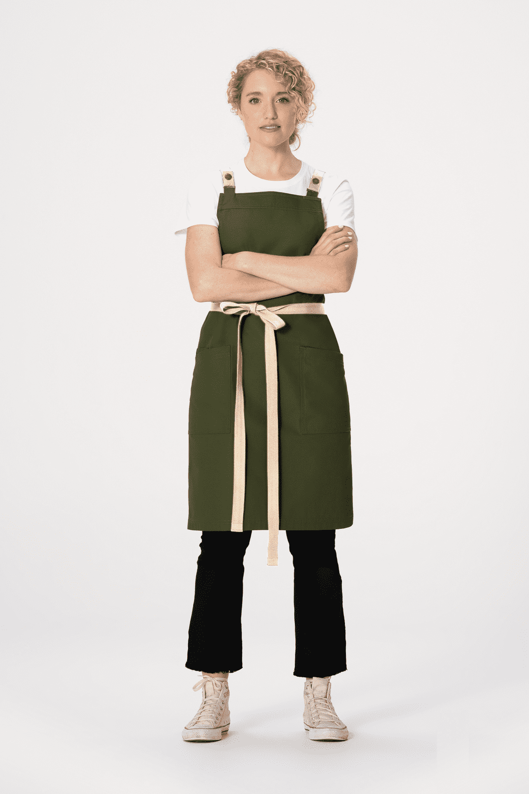 A model wears a green Lockharte Cross Back Apron over a white shirt, paired with black trousers and light-coloured shoes.
