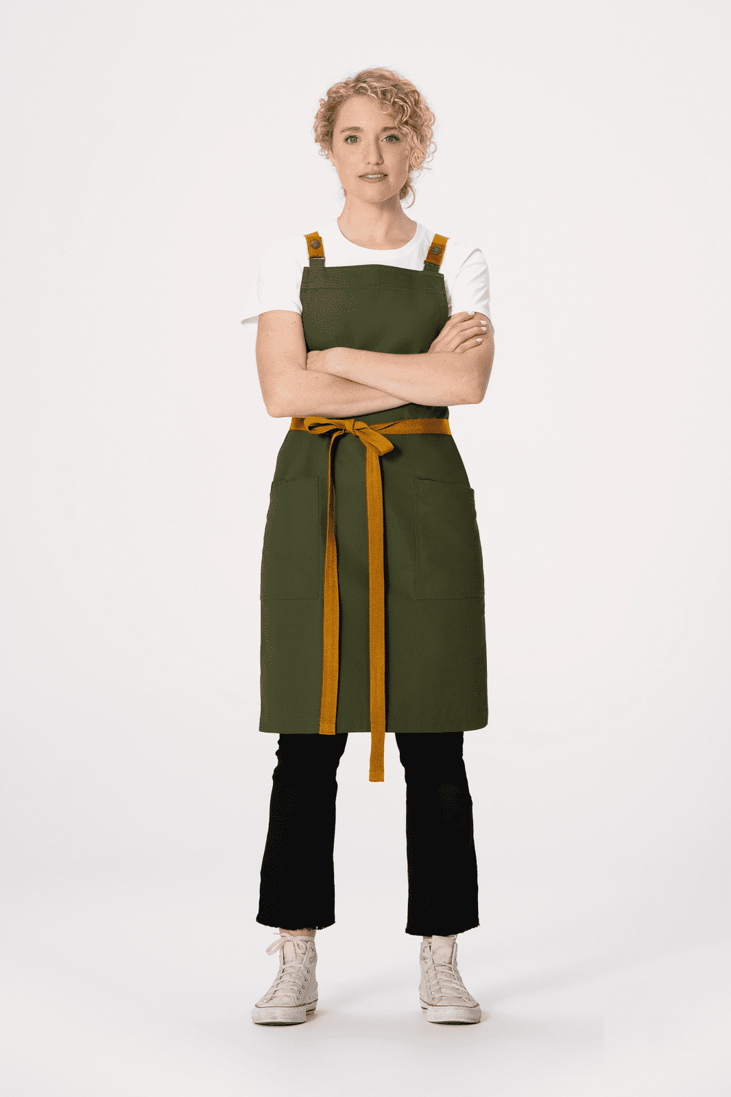 A green cross back apron with a brown tie, worn over a white shirt and black pants, featuring a logo.