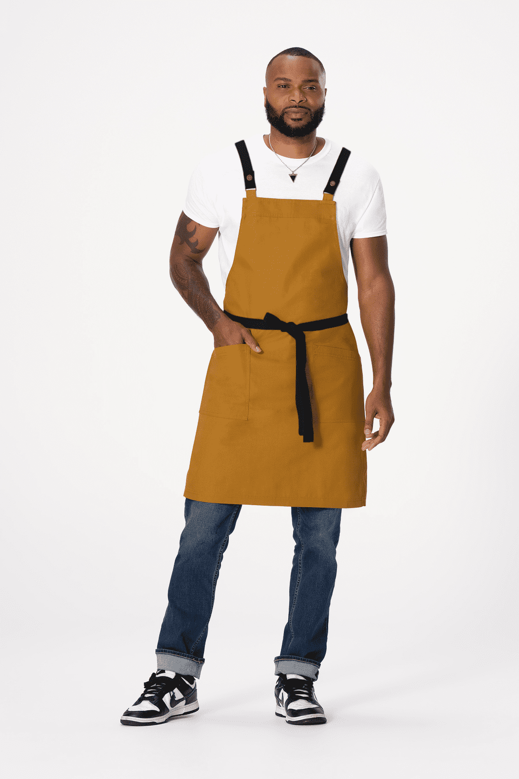 A man wearing a mustard yellow Lockharte cross back apron with a black waist tie, accompanied by jeans and sneakers.