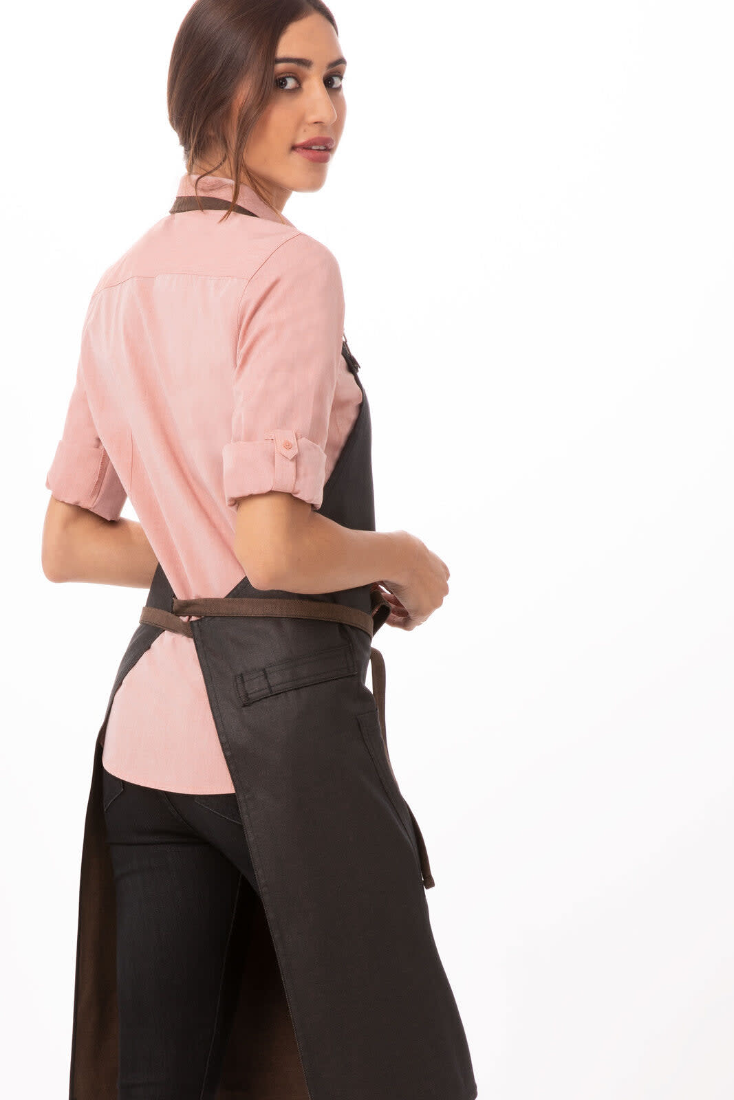 A woman wears a black Boulder Bib Apron over a pink shirt, facing slightly away from the camera.