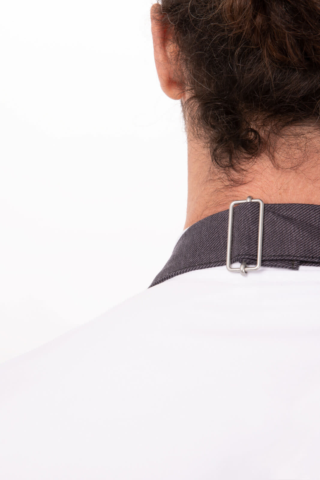 A close-up of the back of a white apron with a dark grey strap and a silver clip attachment.