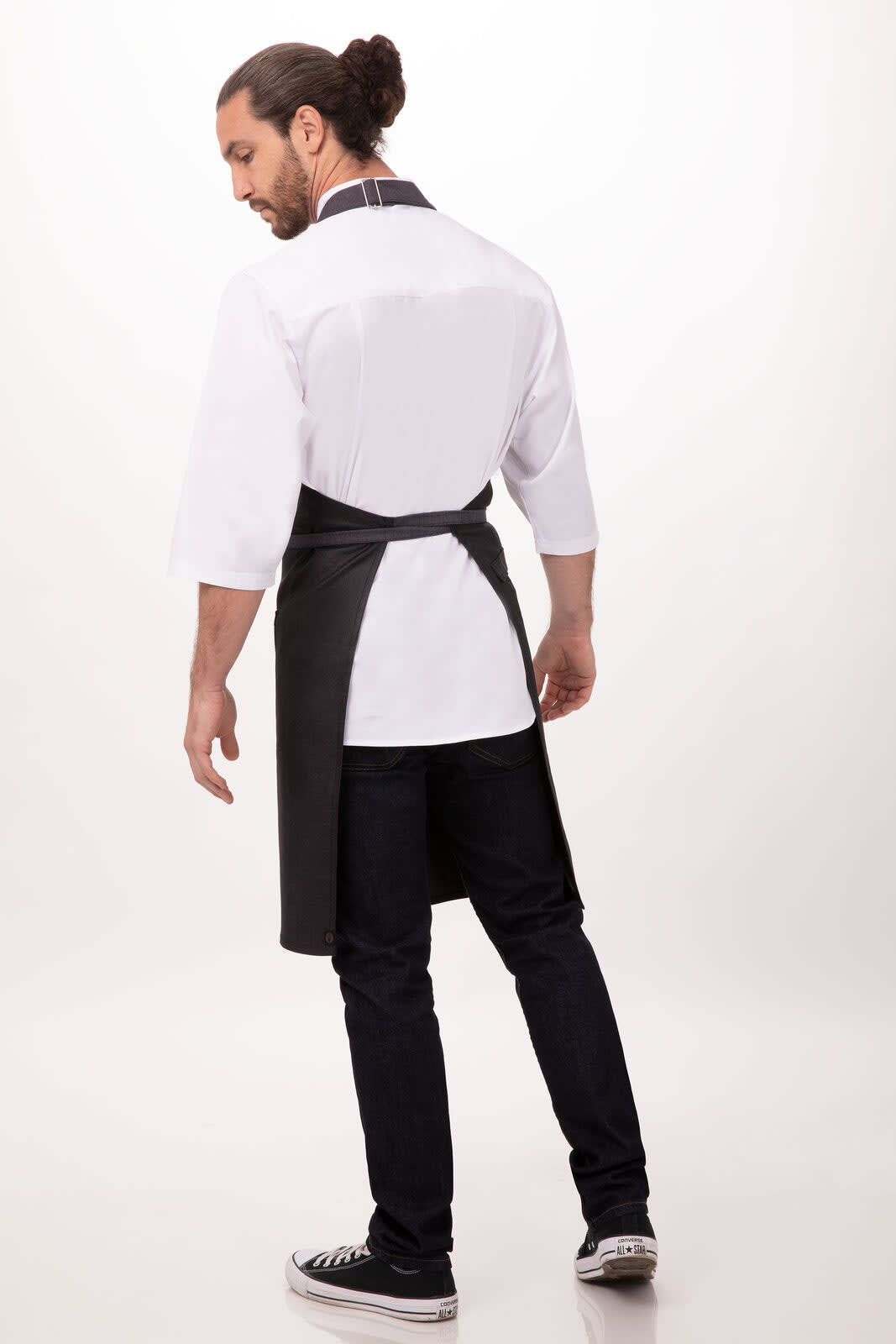 A man wearing a black Boulder Bib Apron over a white shirt and jeans, standing with his back to the camera.