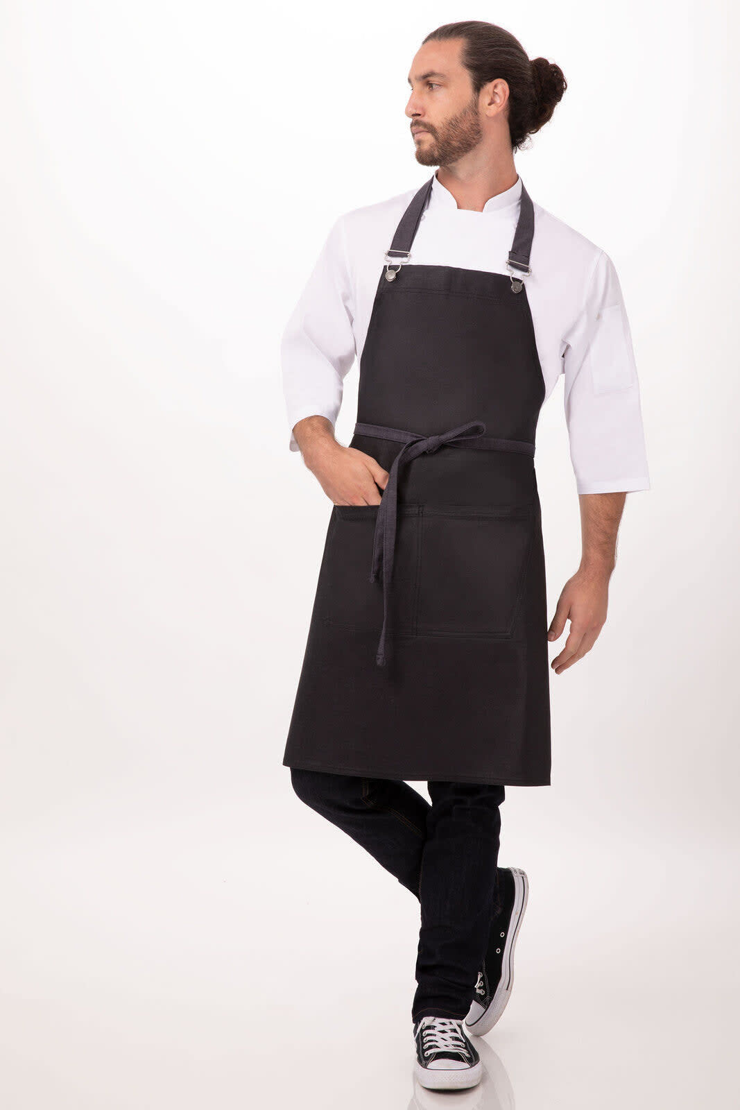 A black bib apron worn by a male model, featuring a pocket and adjustable straps. The model is in casual attire.