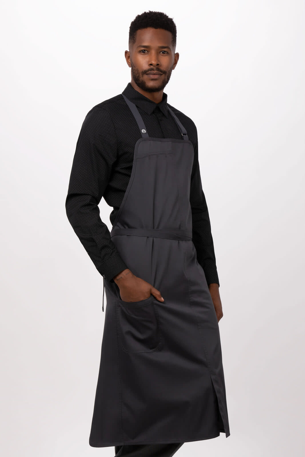 A dark grey bib apron worn by a model, featuring pockets and adjustable straps. It has a logo on the apron.