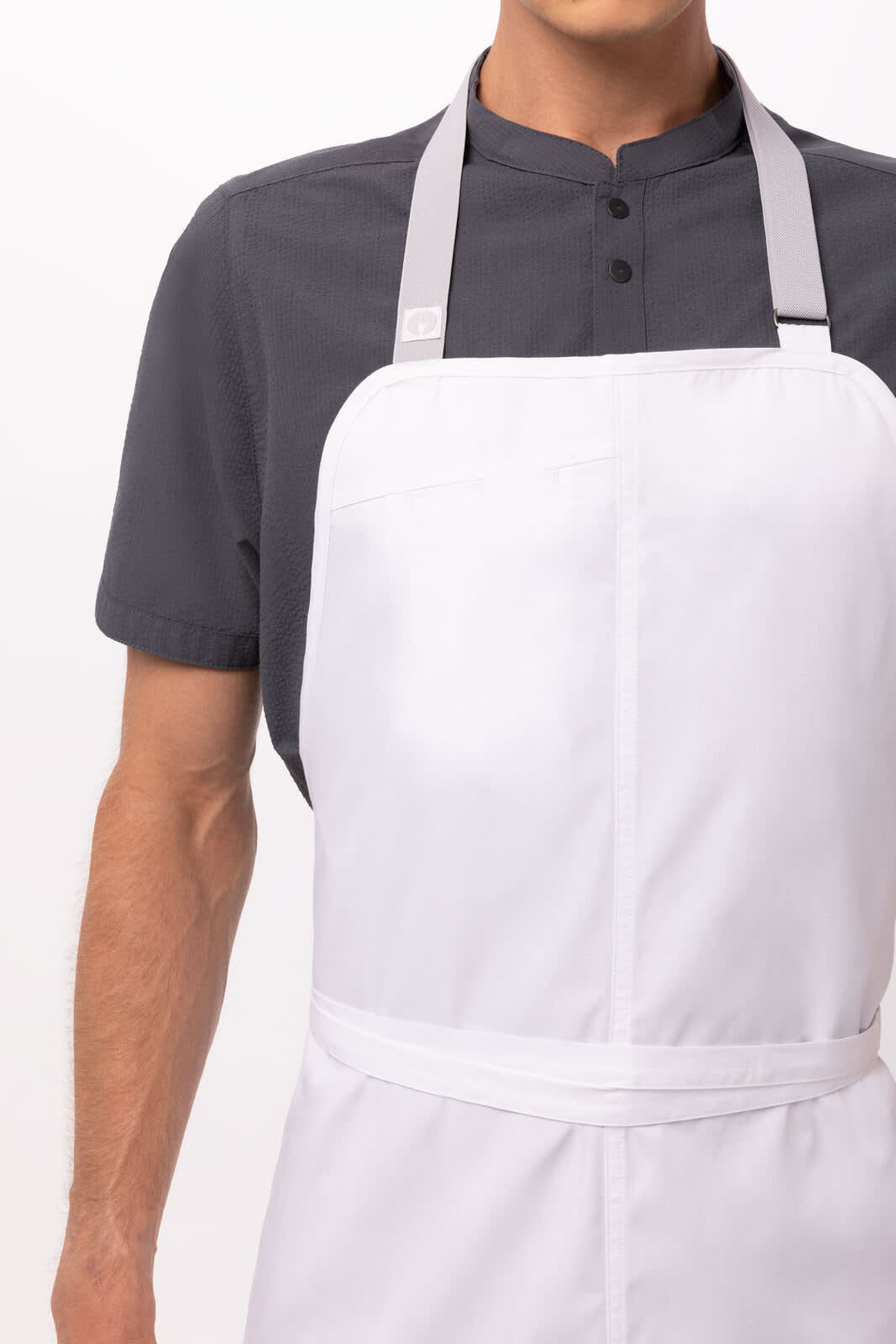 A white bib apron with grey straps worn over a dark grey shirt, featuring a visible logo.