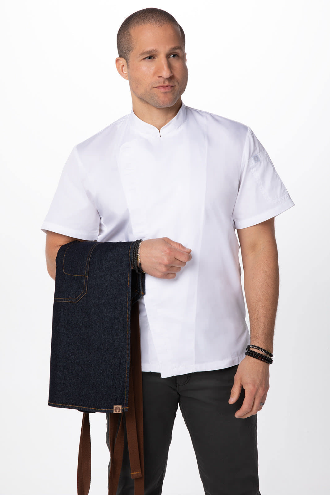 A man in a white shirt holds a navy denim cross back apron, featuring brown straps and a logo.