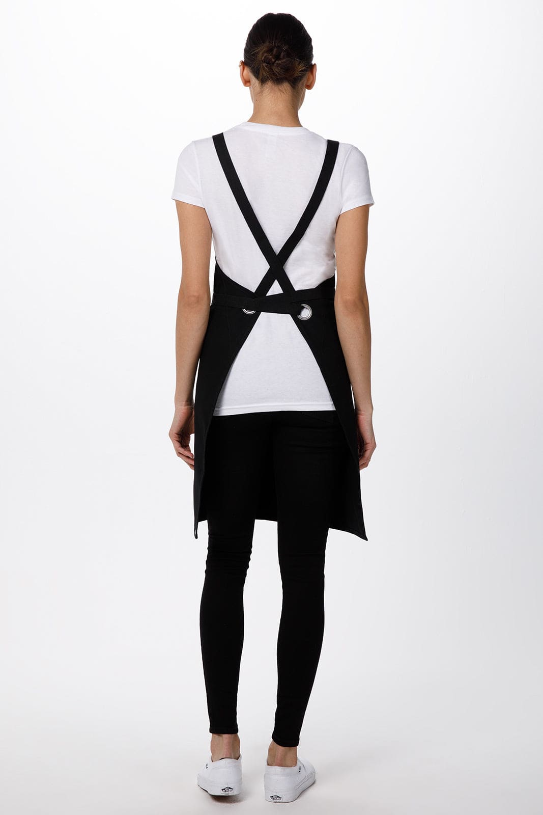 A black Byron Cross-Back Apron featuring a stylish strap design, shown worn by a model from the back.