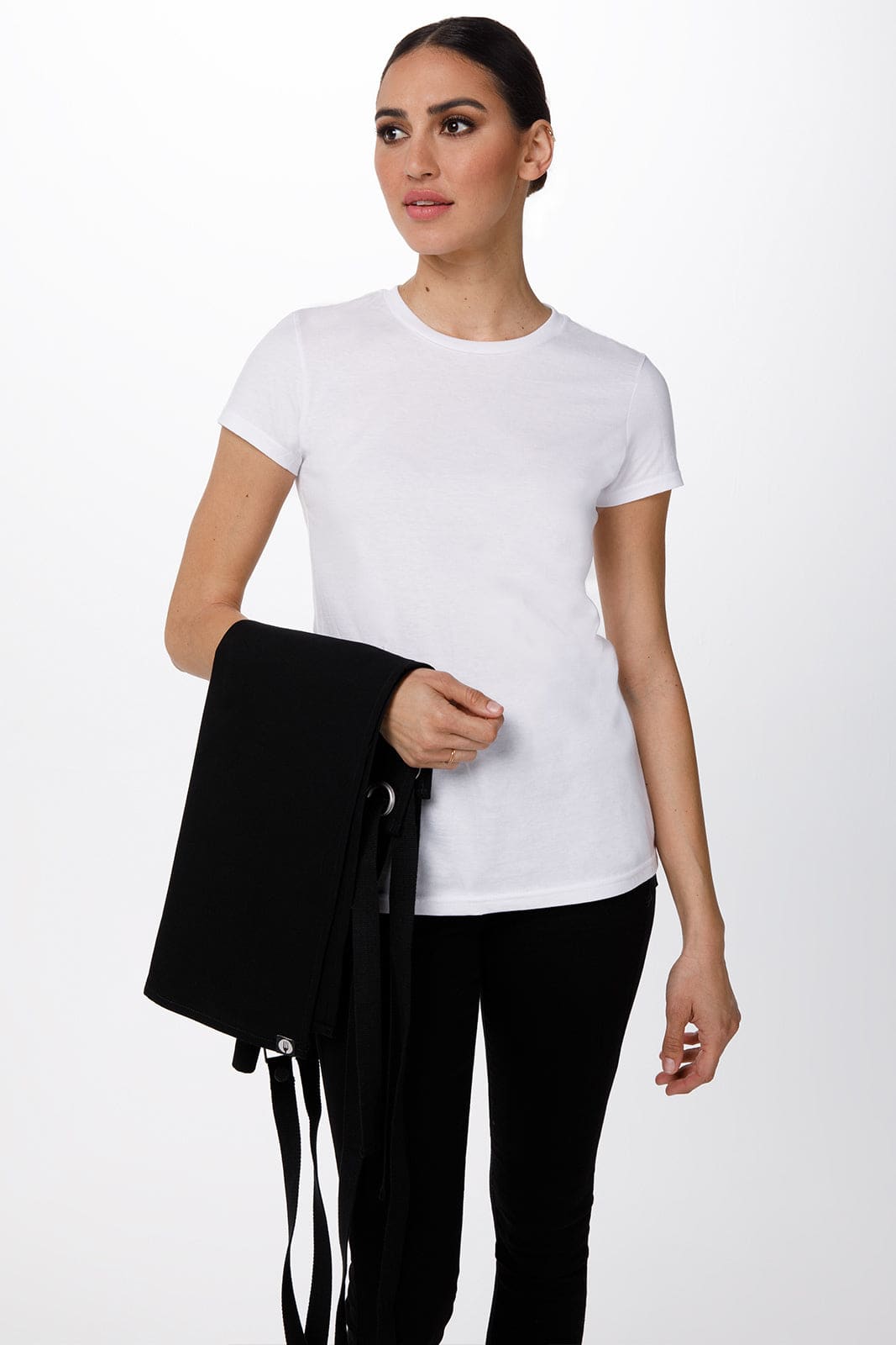 A woman in a white t-shirt holds a black Byron Cross-Back Apron. The apron features long ties for fastening.