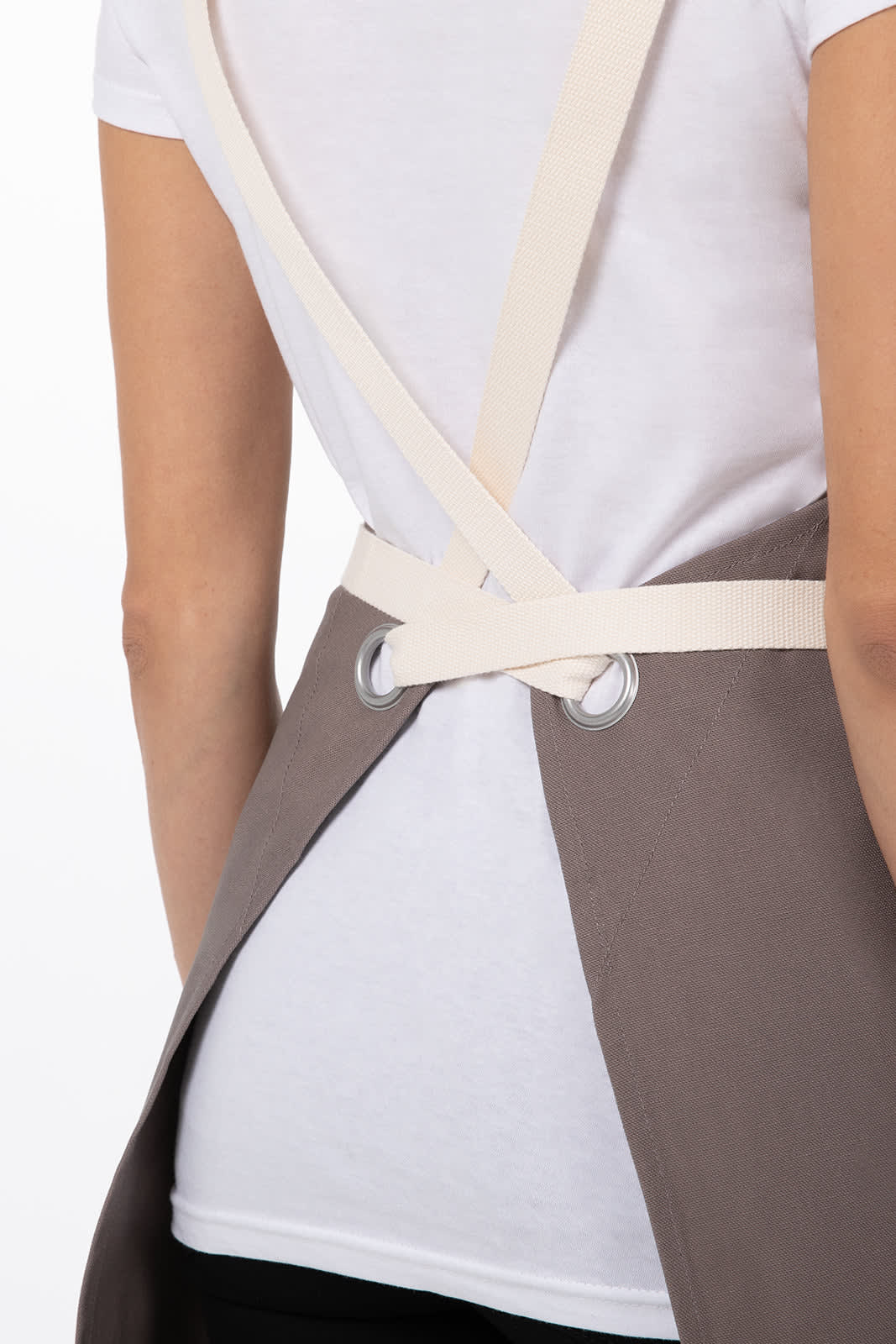 A brown cross-back apron with cream straps, featuring an eyelet design at the back.