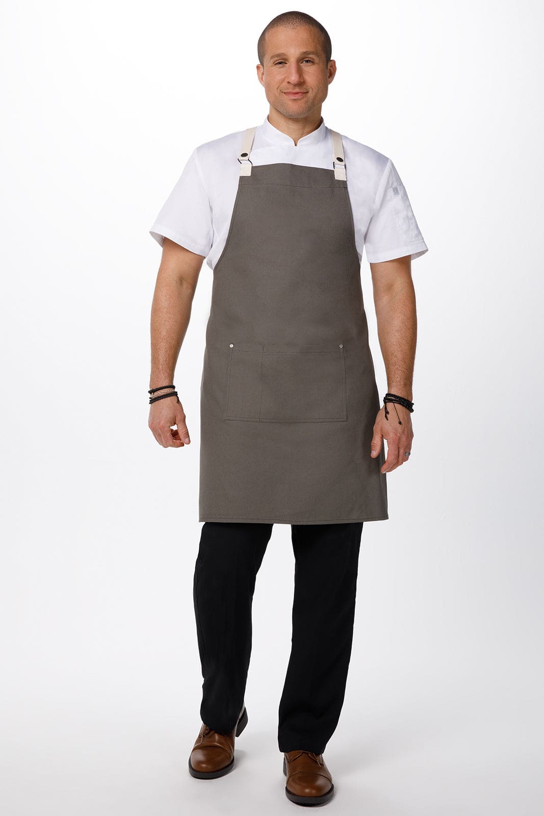 A man wearing a grey Byron Cross-Back Apron over a white shirt, standing with hands at his sides. The apron features a logo.