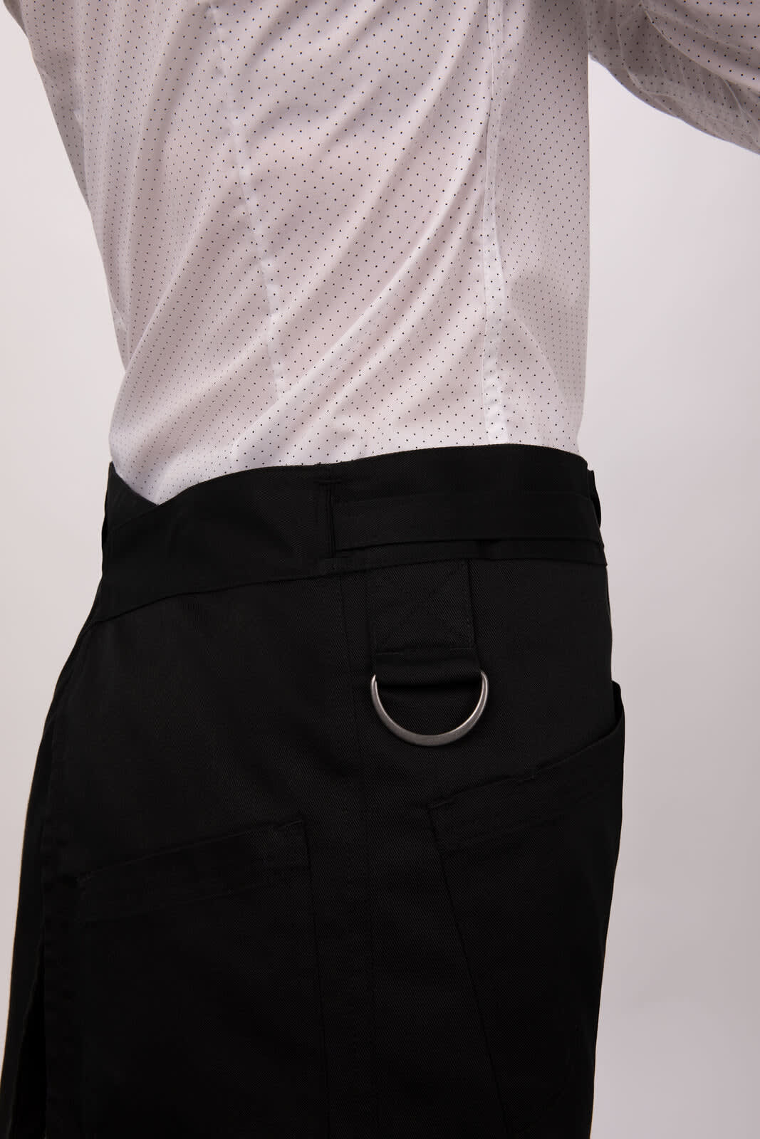 A black half bistro apron featuring a silver metal ring, worn on a person in a white shirt.