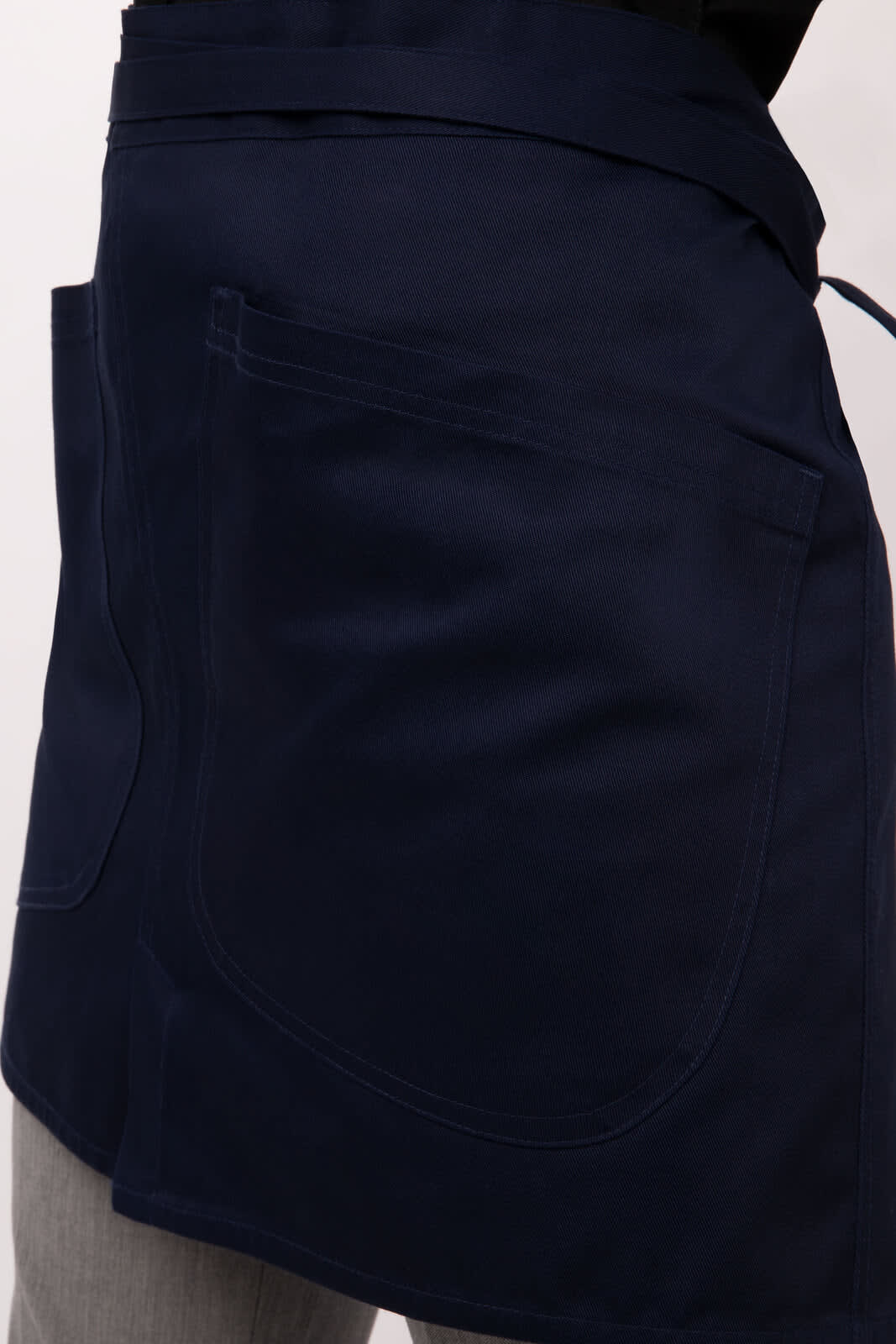 A navy half bistro apron featuring two spacious pockets and a tie at the waist, displayed on a model.