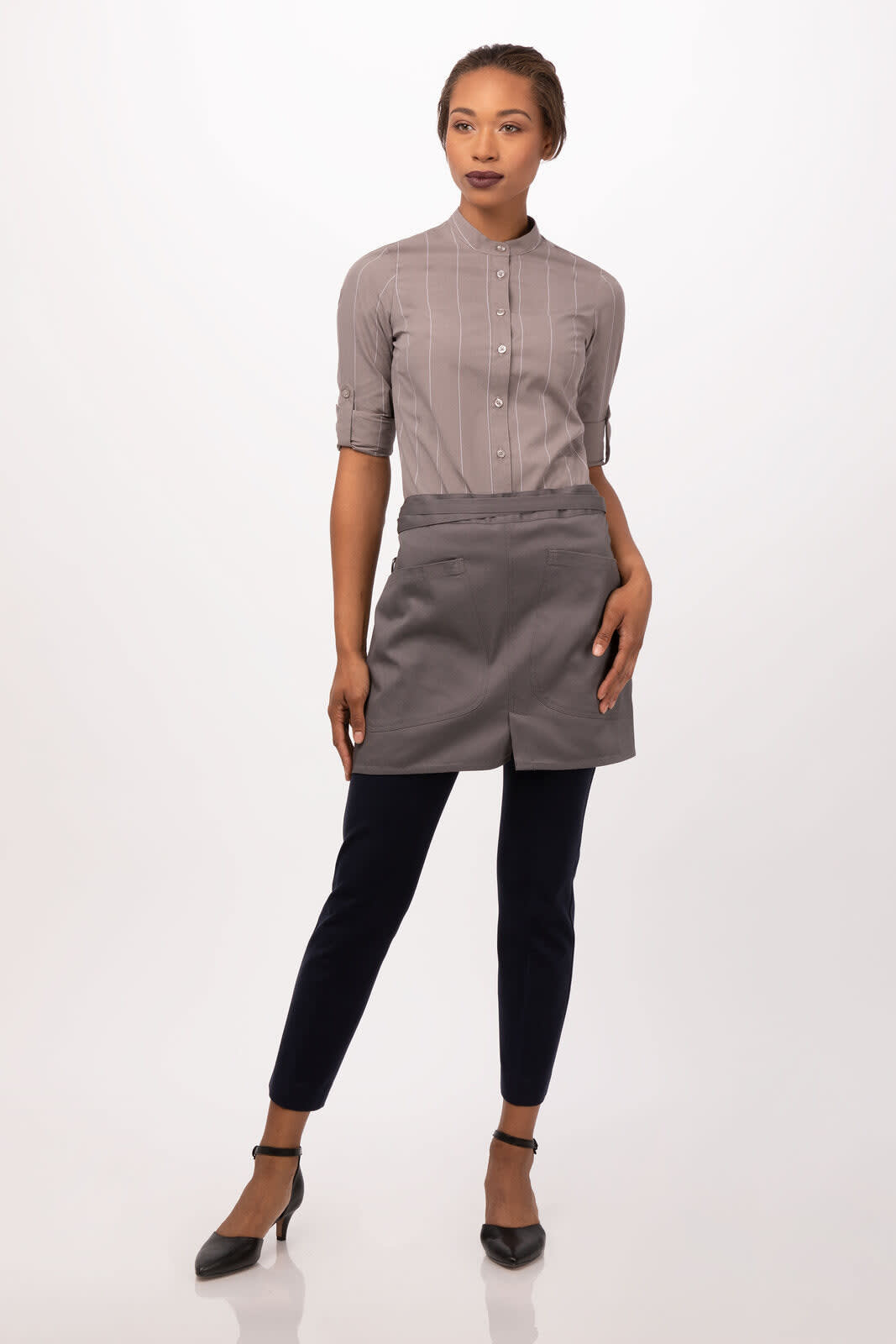 A grey half bistro apron worn over a button-up shirt, modelled with dark pants and heels. The apron has a logo.
