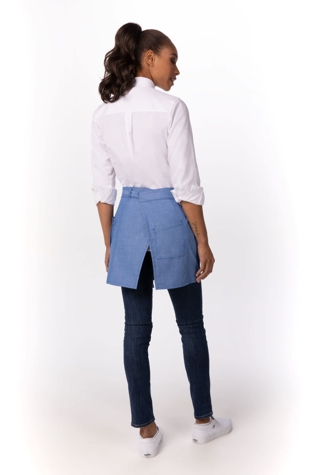 A woman wears a blue half bistro apron over a white shirt and blue jeans, with her back facing the camera.