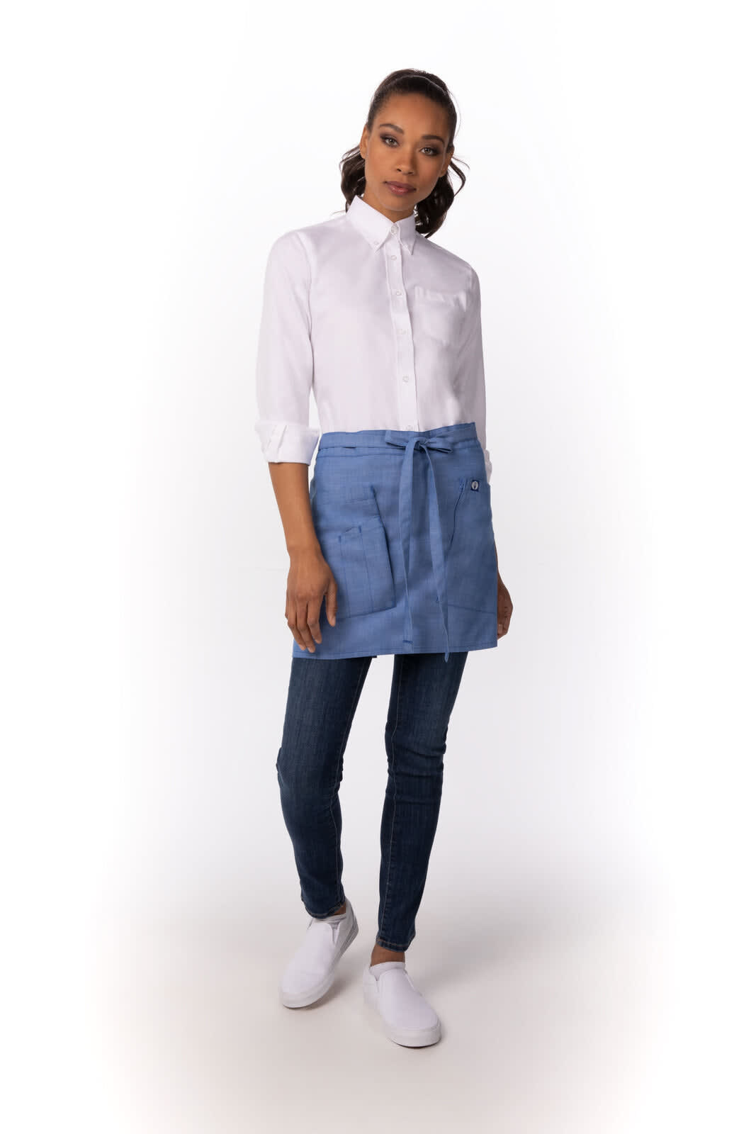 A model wearing a blue half bistro apron over a white shirt and jeans, paired with white shoes. 