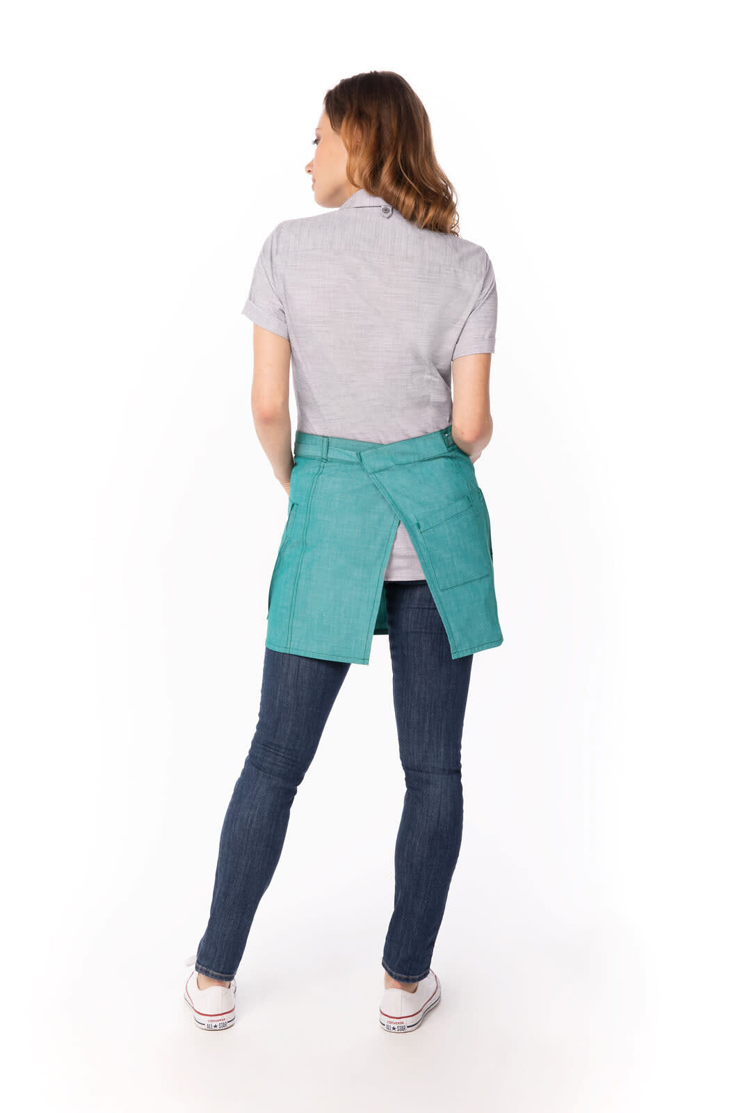 A woman wearing a teal bistro apron, viewed from the back, paired with a grey shirt and dark jeans.