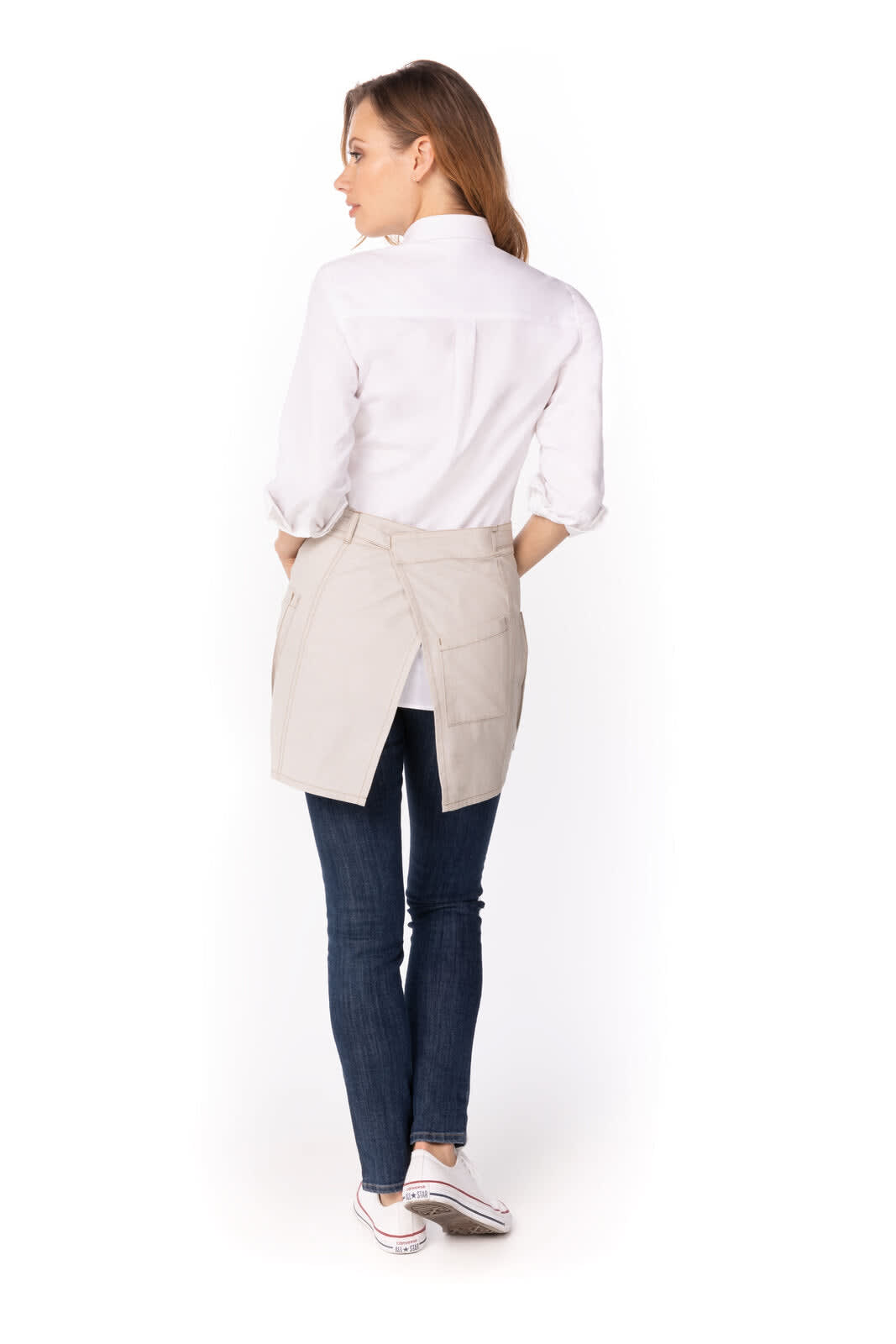 A woman wearing a light beige half bistro apron over a white shirt, paired with blue jeans and sneakers.
