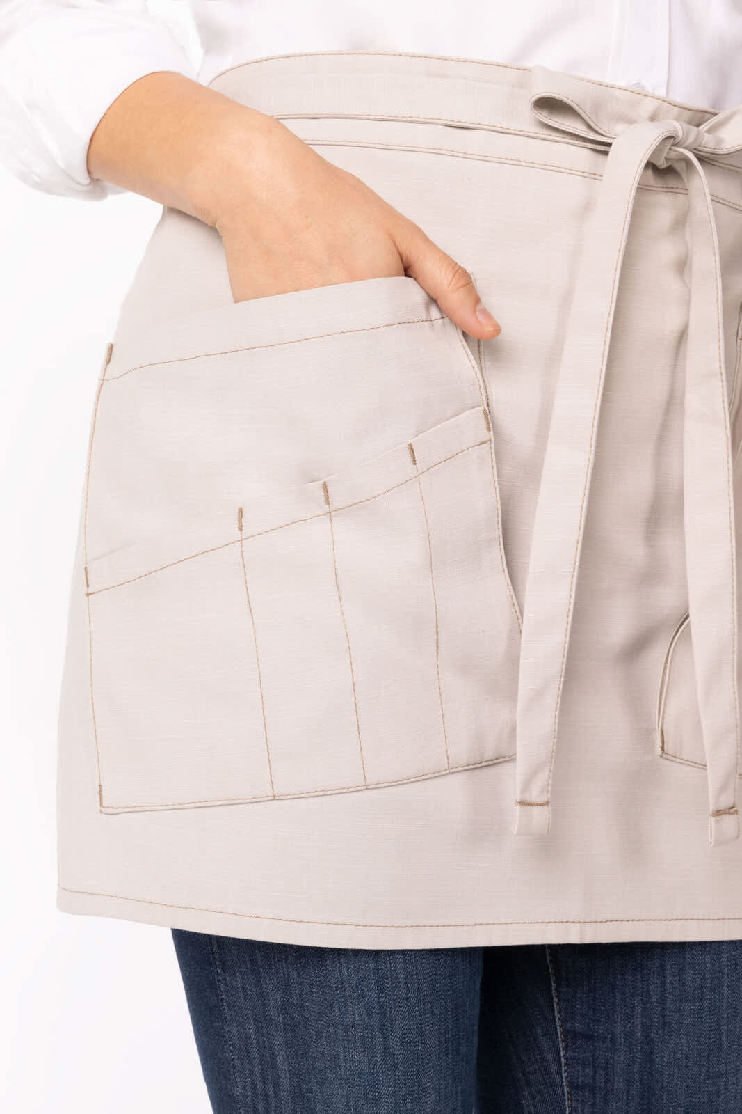 A beige half bistro apron with a large front pocket and ties, worn over denim jeans. The apron features a logo.