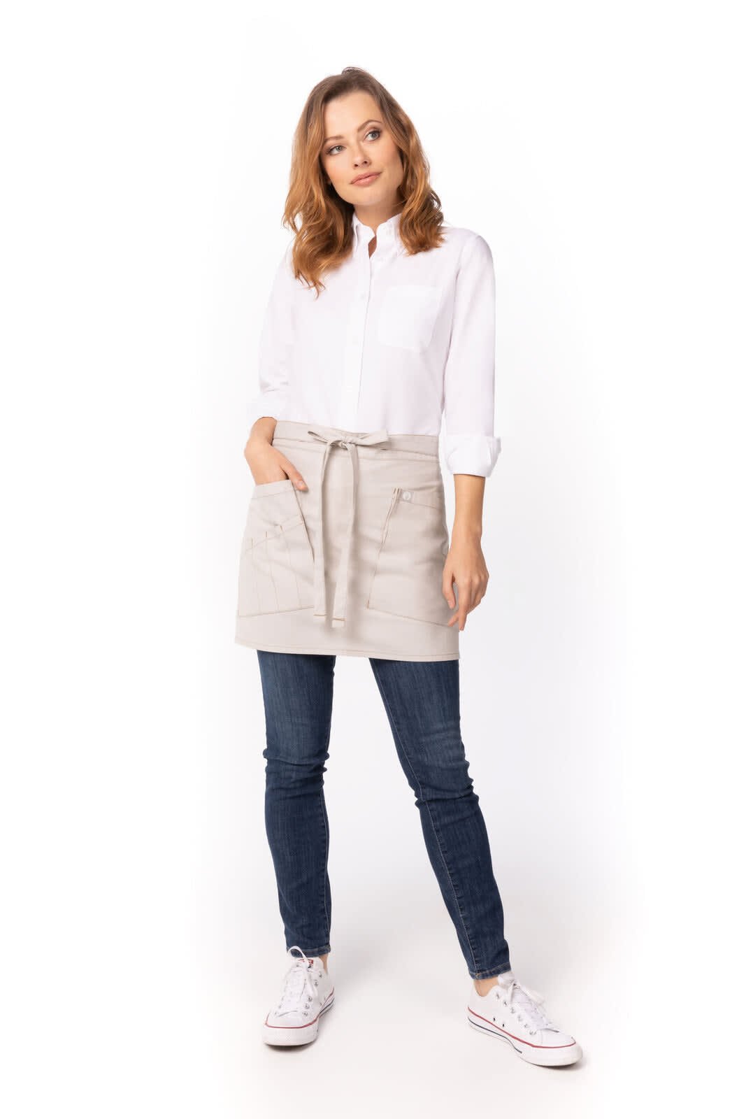 A model wears a beige bistro apron over a white shirt and blue jeans, paired with white shoes. The apron features a logo.