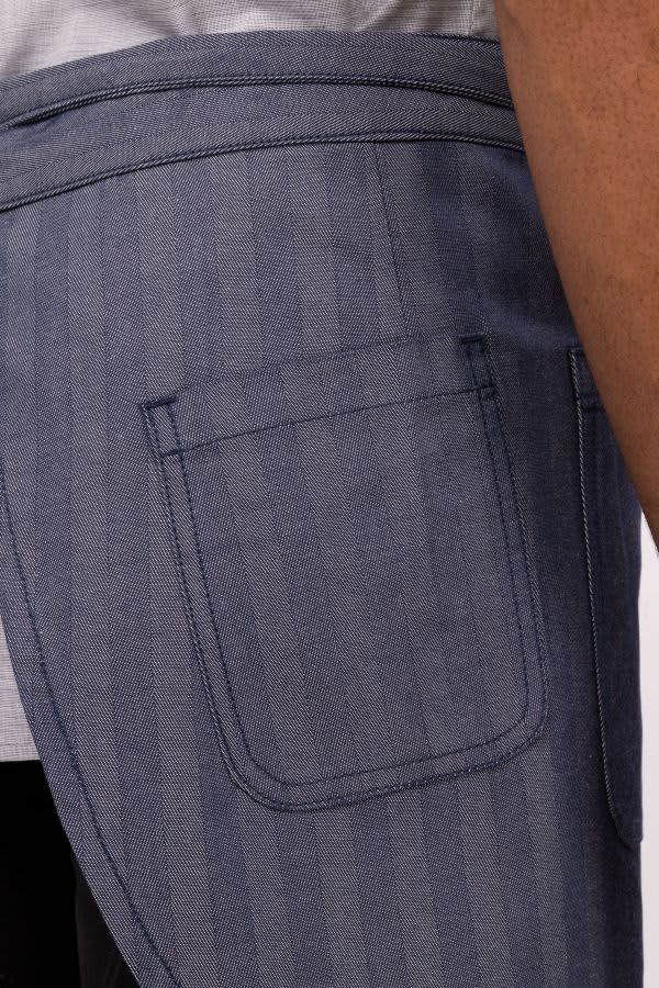 A half bistro apron in blue with a pocket, designed for workwear. Features a subtle striped pattern.