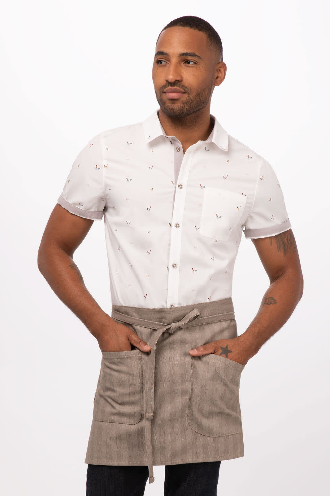A man wearing a white patterned shirt and a light brown bistro apron featuring pockets and a tie. The apron has a logo.