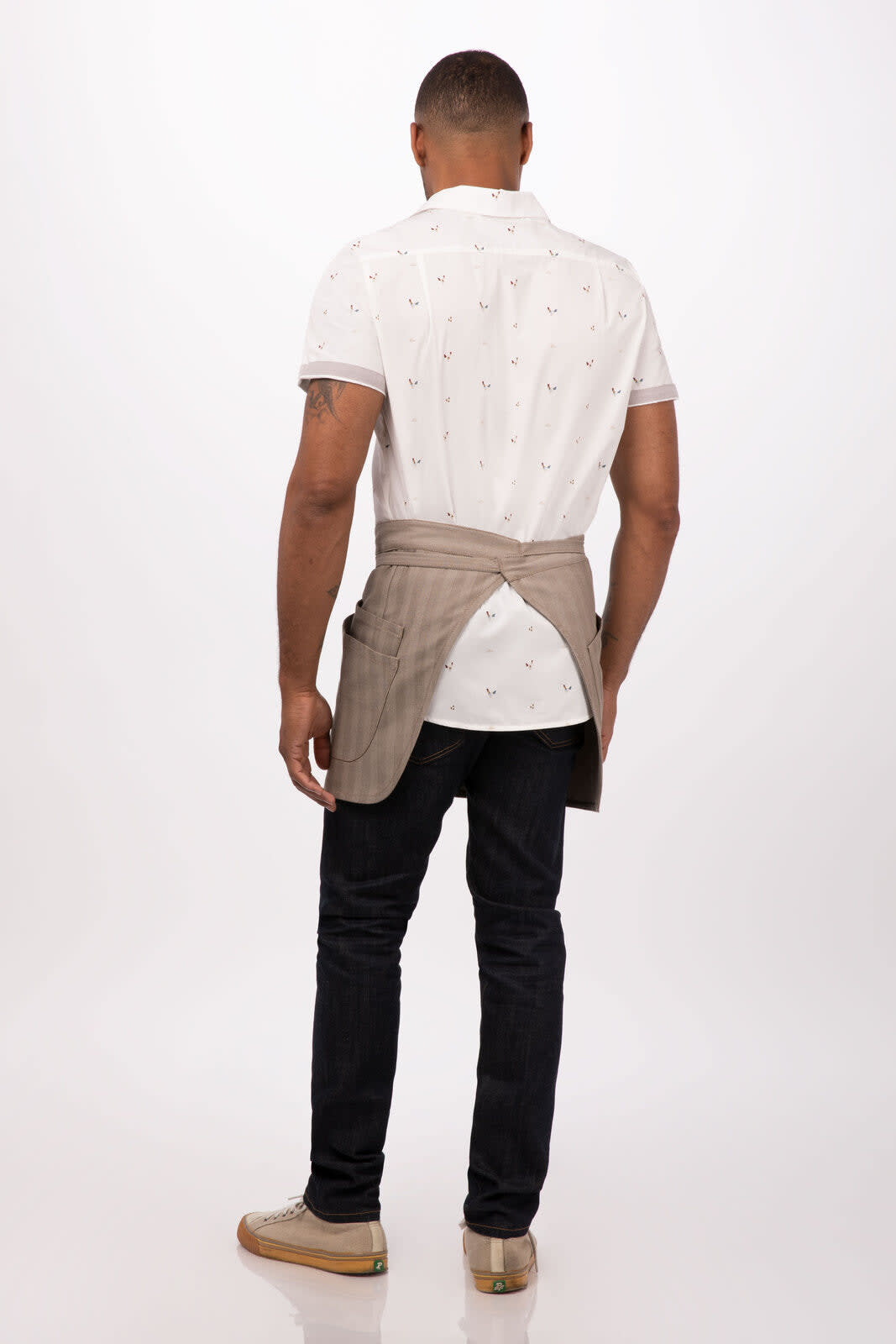 A bistro apron in a light brown colour, worn over a patterned shirt, with a plain background. The apron has a logo.