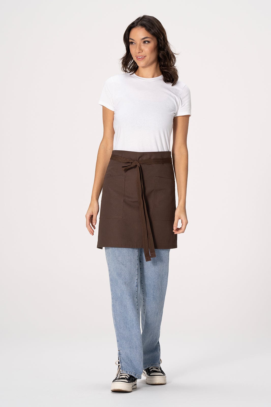 A woman models a brown Lockharte waist apron over a white shirt and blue jeans, featuring a tie at the waist.