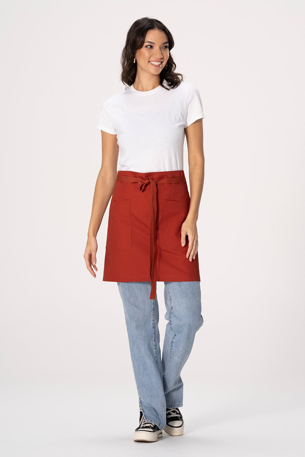 A woman wearing a red waist apron over a white t-shirt and blue jeans, standing against a light background.