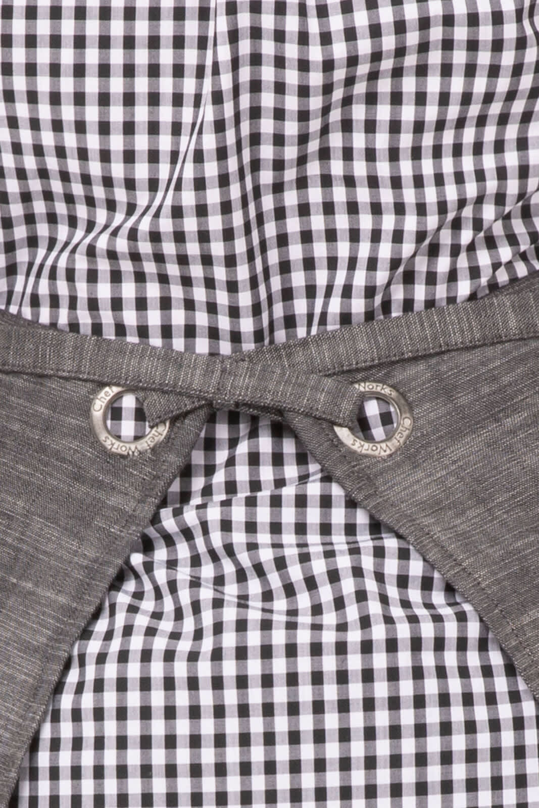 A bistro apron featuring a grey fabric and a black and white checked pattern, with decorative silver eyelets.