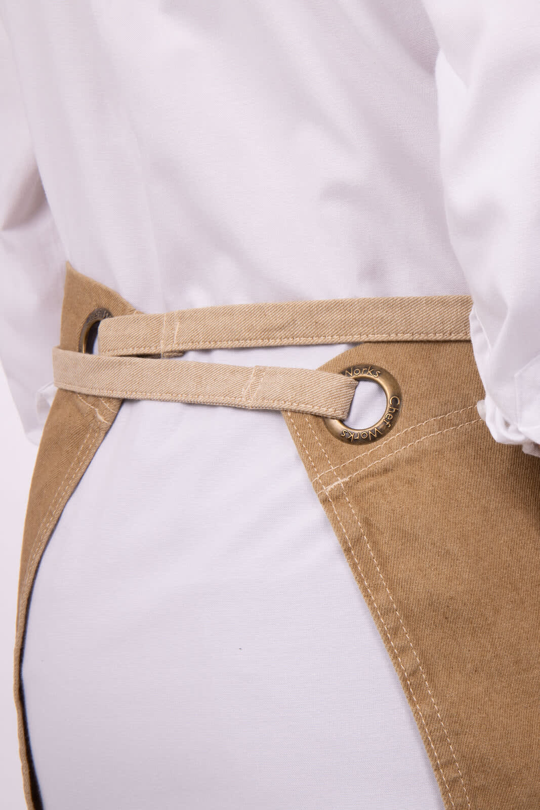 A beige bistro apron with a waist tie and metal eyelets, designed for workwear.