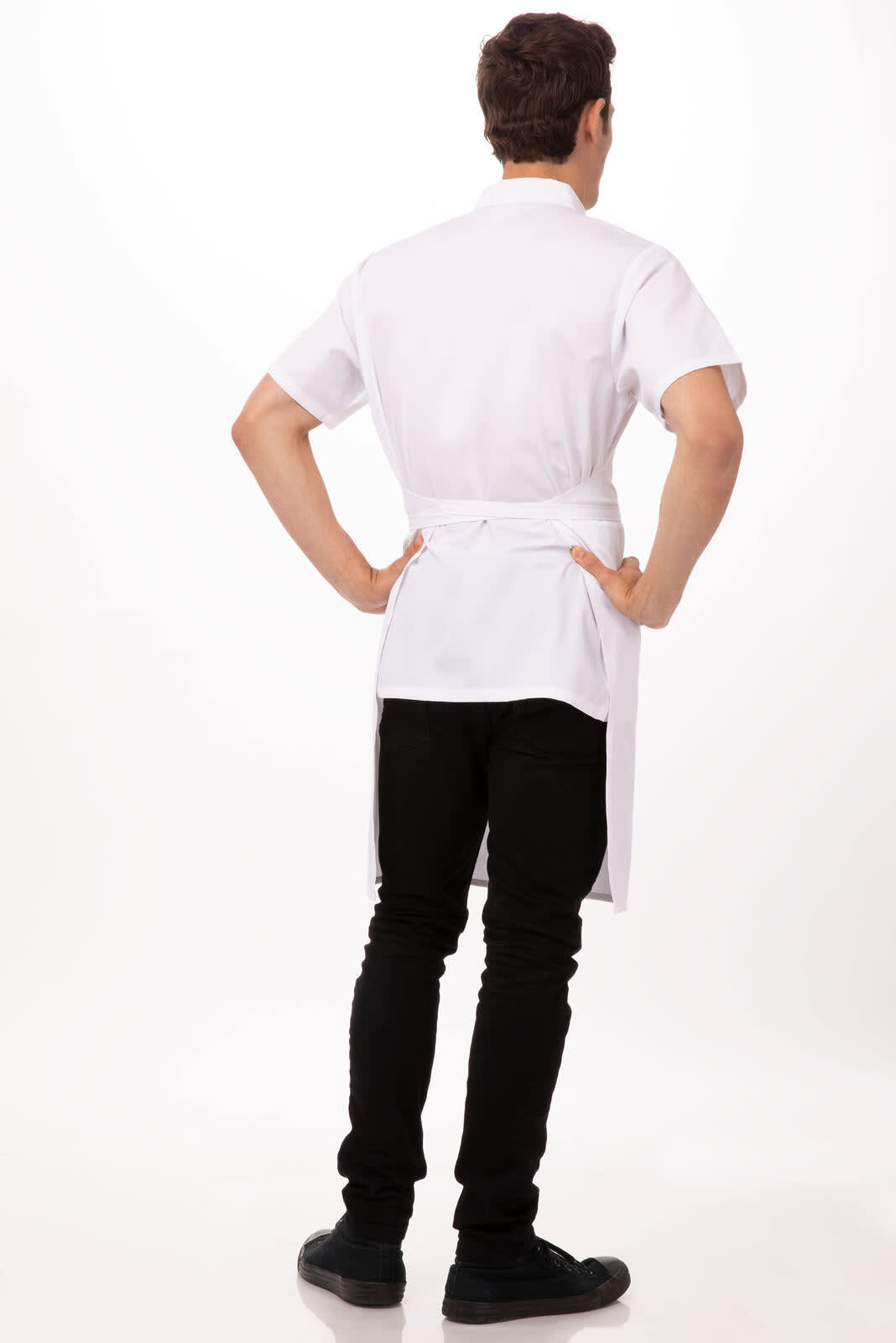 A white bib apron worn by a person, featuring short sleeves and tied at the back, paired with black pants and shoes.
