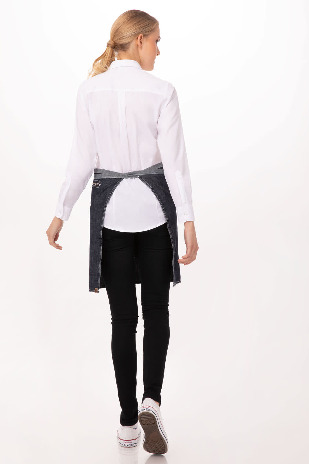 A woman in a white shirt and black pants wears a navy blue bistro apron, seen from the back.