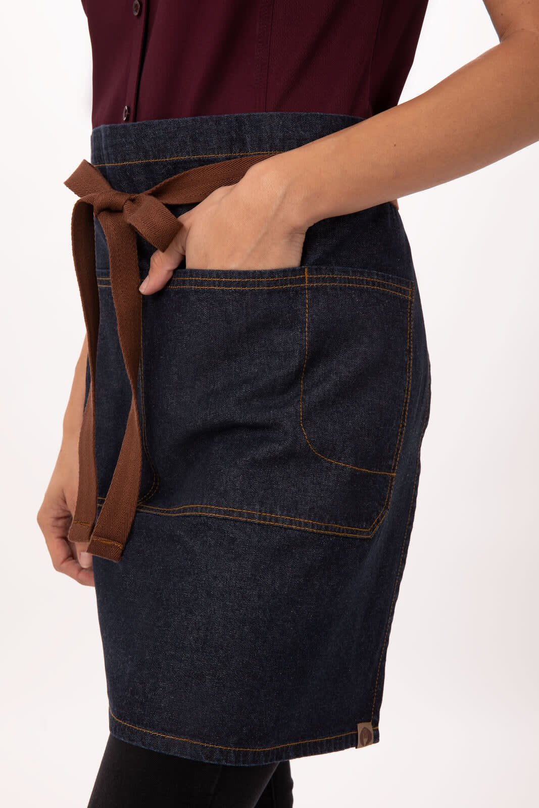A dark denim bistro apron with a brown tie and pockets, displayed on a model. It features visible stitching details.