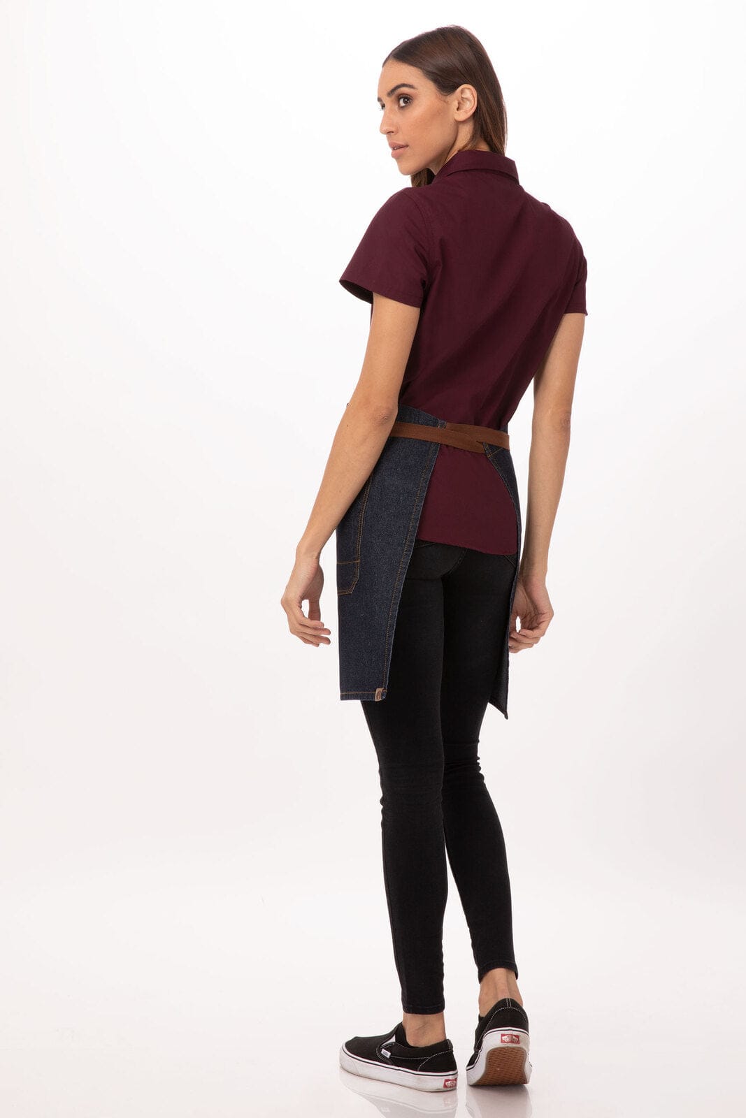 A woman in a maroon short-sleeve shirt wears a denim half bistro apron, paired with black leggings and shoes.