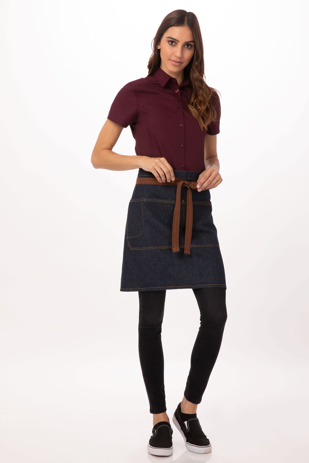 A bistro apron in a dark denim colour, featuring a brown tie and pockets, styled with a maroon shirt and black pants.