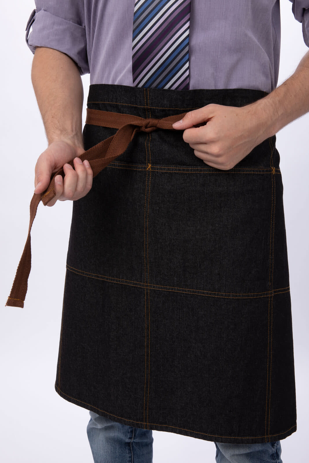 A dark denim apron with brown ties, worn by a person who is tying it around their waist.