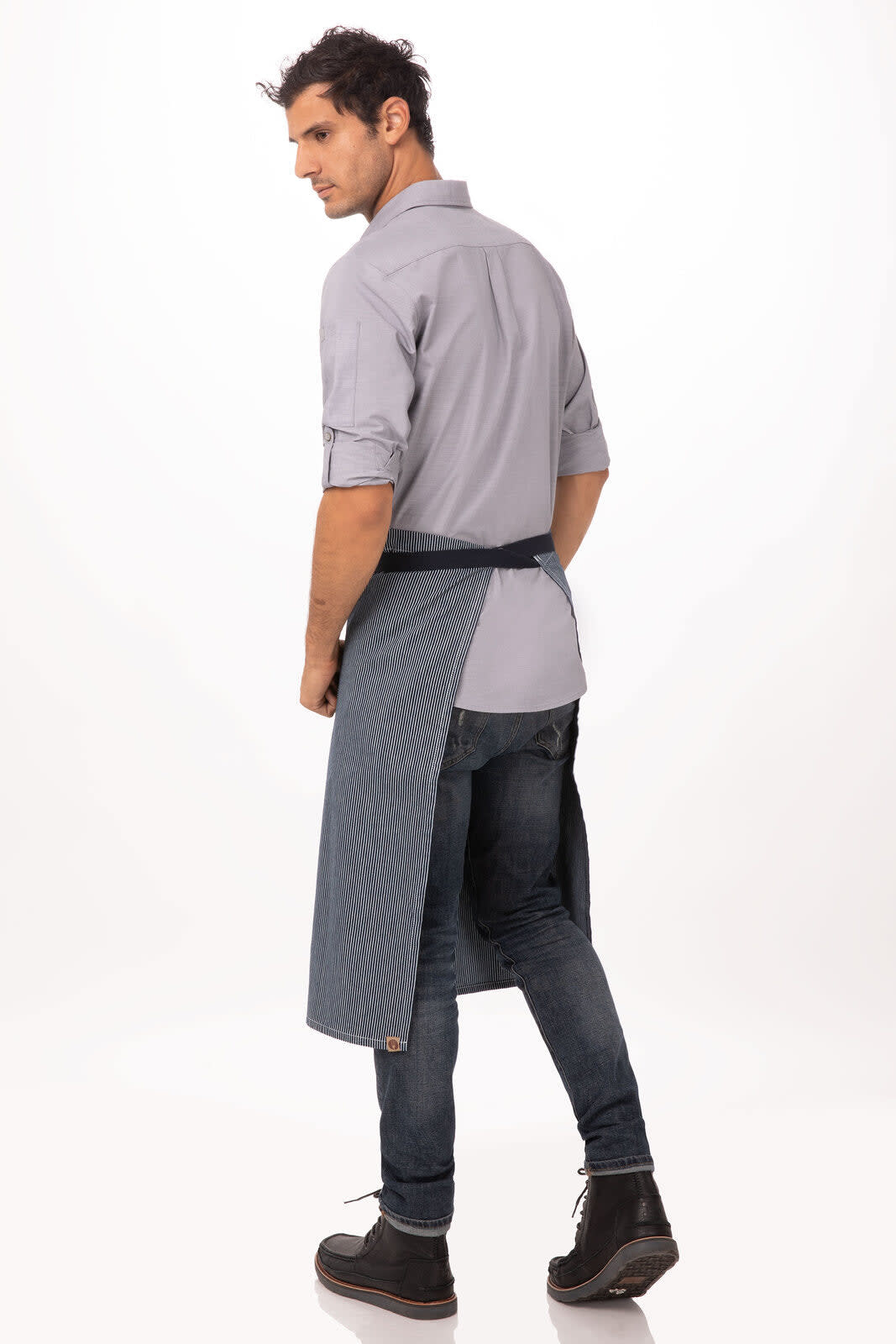 A man in a grey shirt and dark jeans wears a blue denim Portland Bistro Apron, showcasing its stylish design.