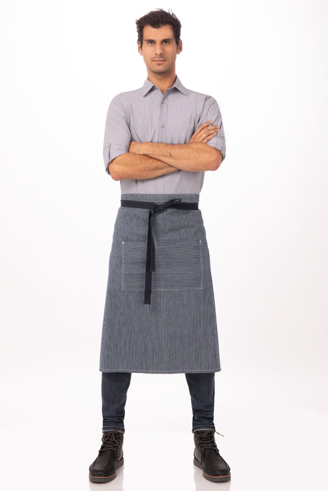 A man wearing a striped blue apron over a grey shirt, standing with arms crossed. The apron features a logo.