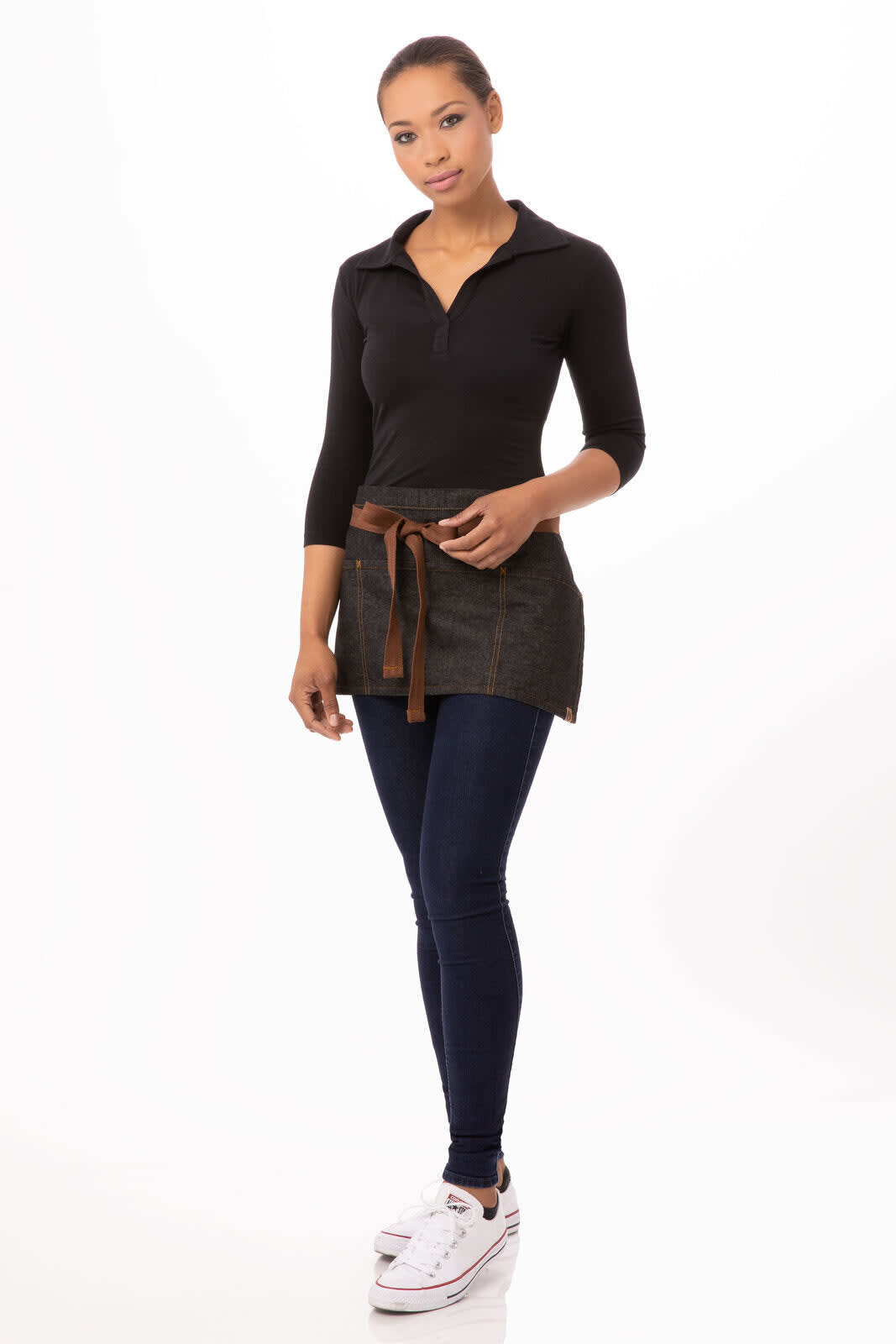 A model wearing a dark grey Memphis waist apron with a brown tie, paired with jeans and sneakers.